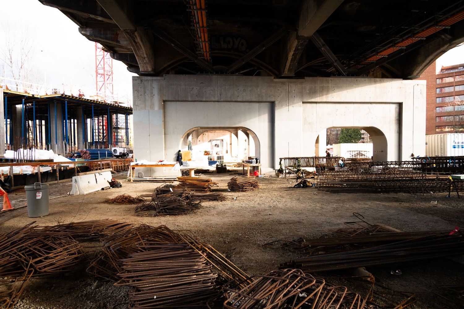 Under-bridge construction site with steel rebar piles and concrete arch supports in urban setting.