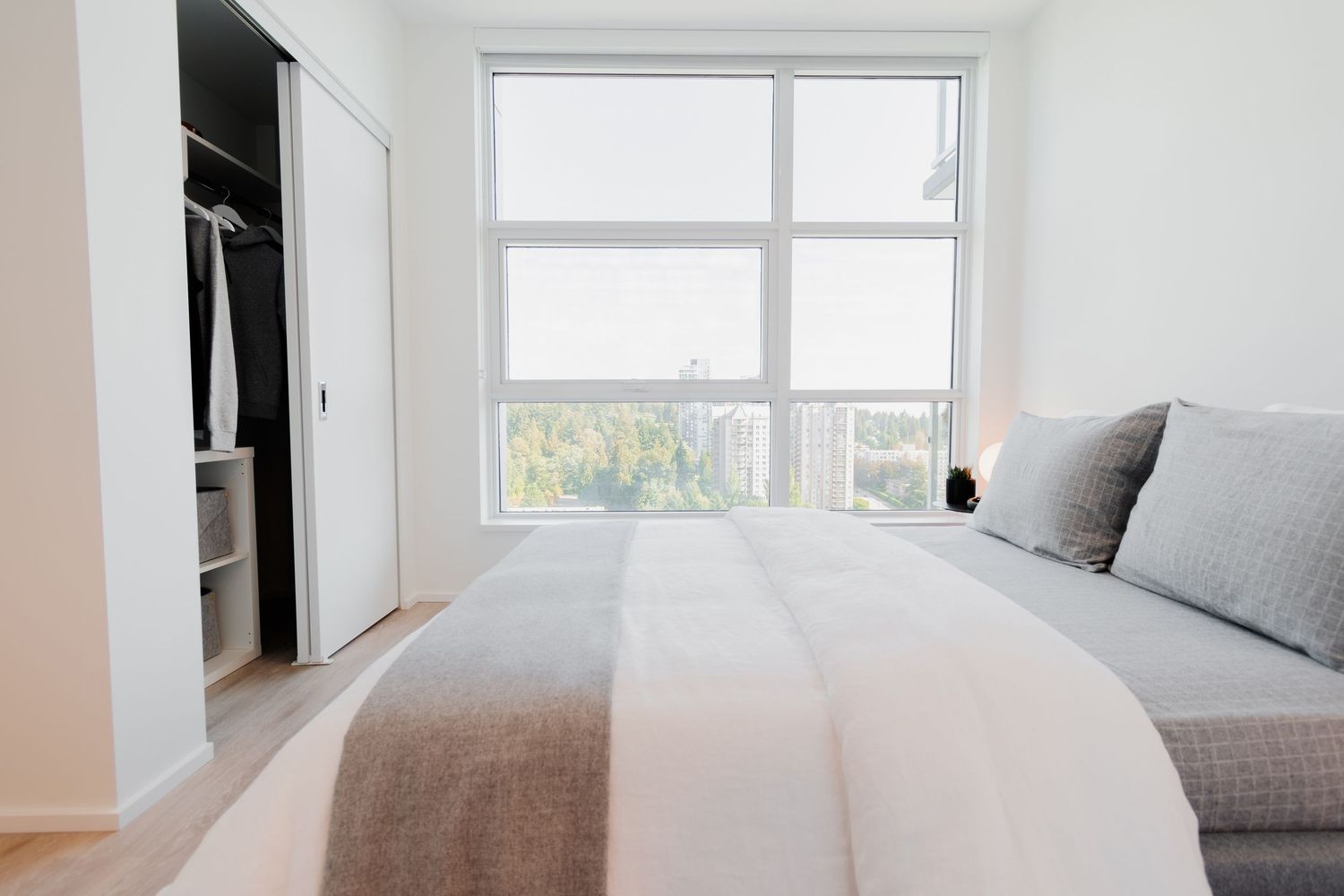 Bright minimalist bedroom with large window, walk-in closet, and neutral bedding in a modern condo.
