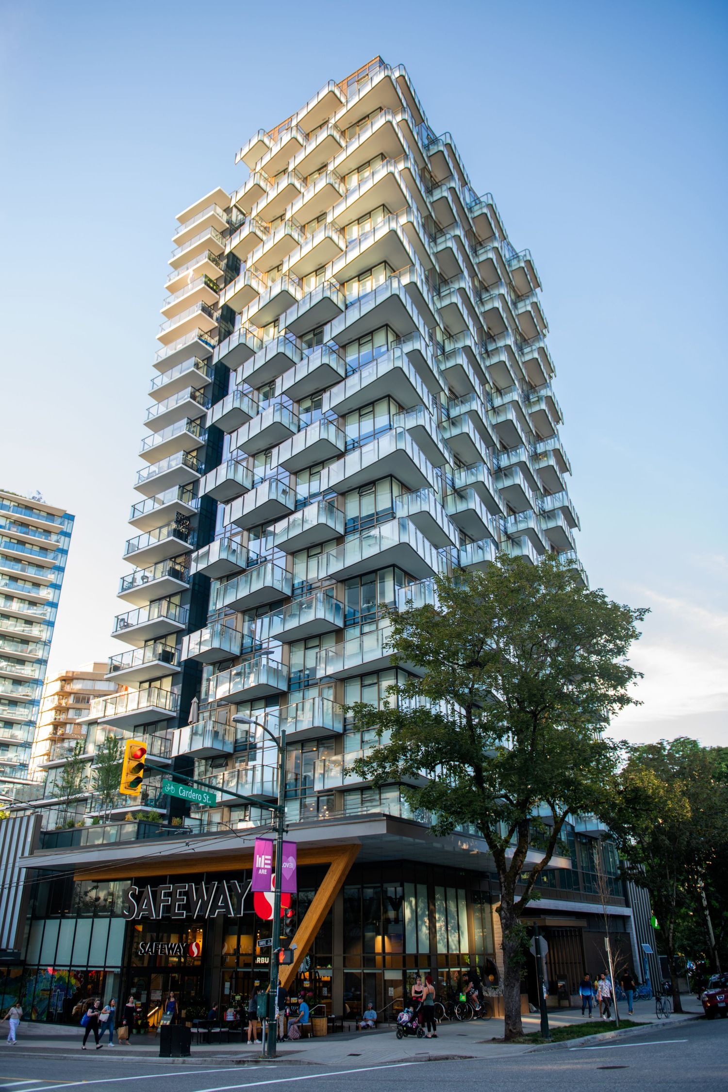 Modern luxury high-rise residential tower with unique staggered balconies above street-level Safeway grocery store.