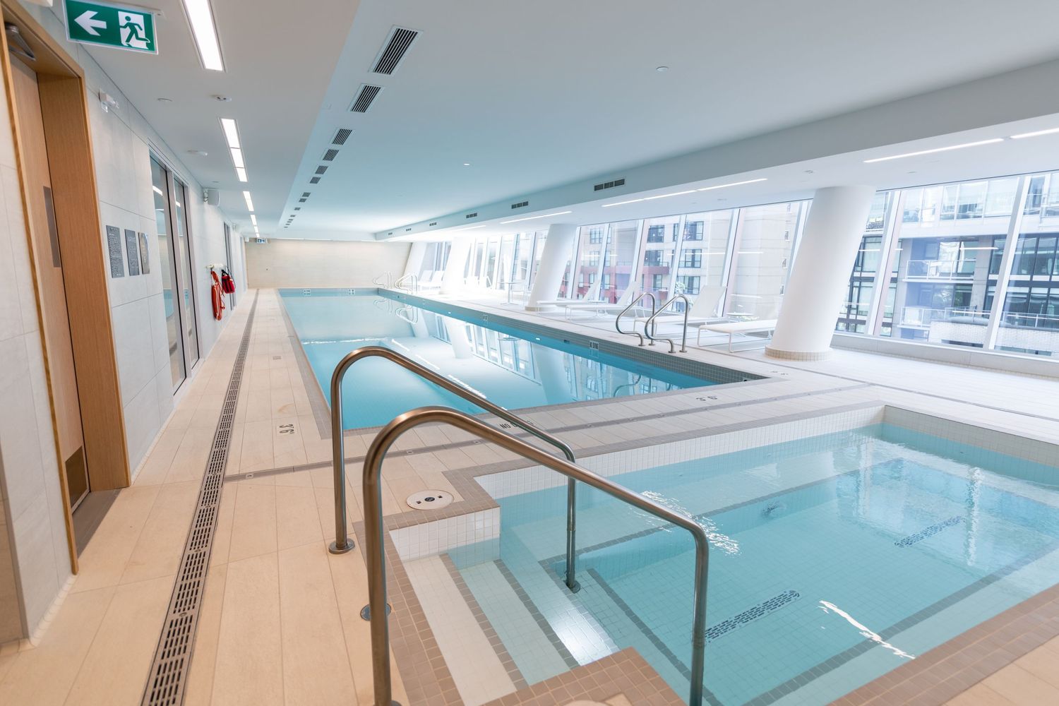 Indoor lap pool with handrails and a hydrotherapy pool in a modern aquatic facility with large windows.