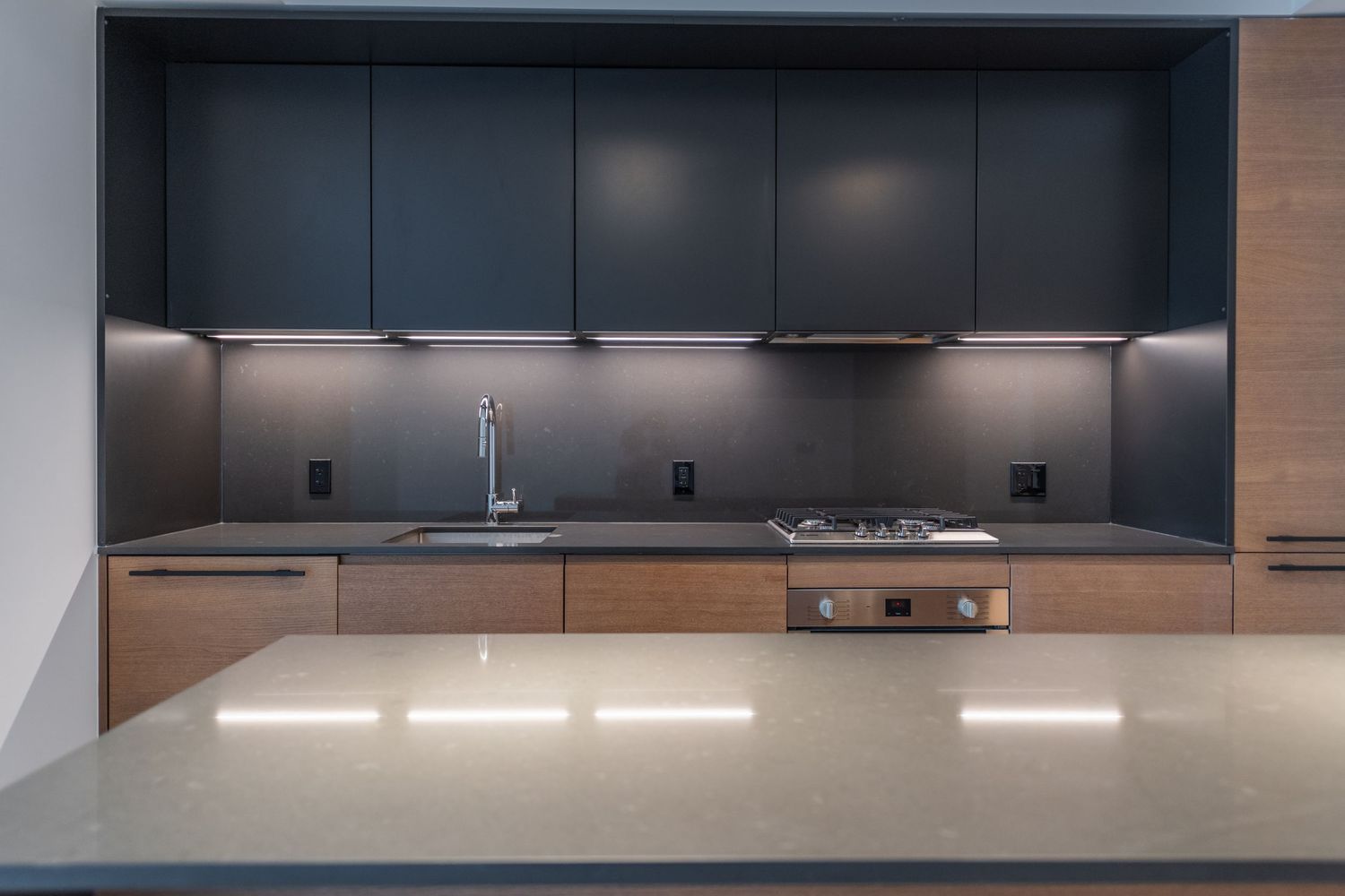 Sleek modern kitchen with dark navy upper cabinets, wood lower cabinets, and a stone waterfall island.