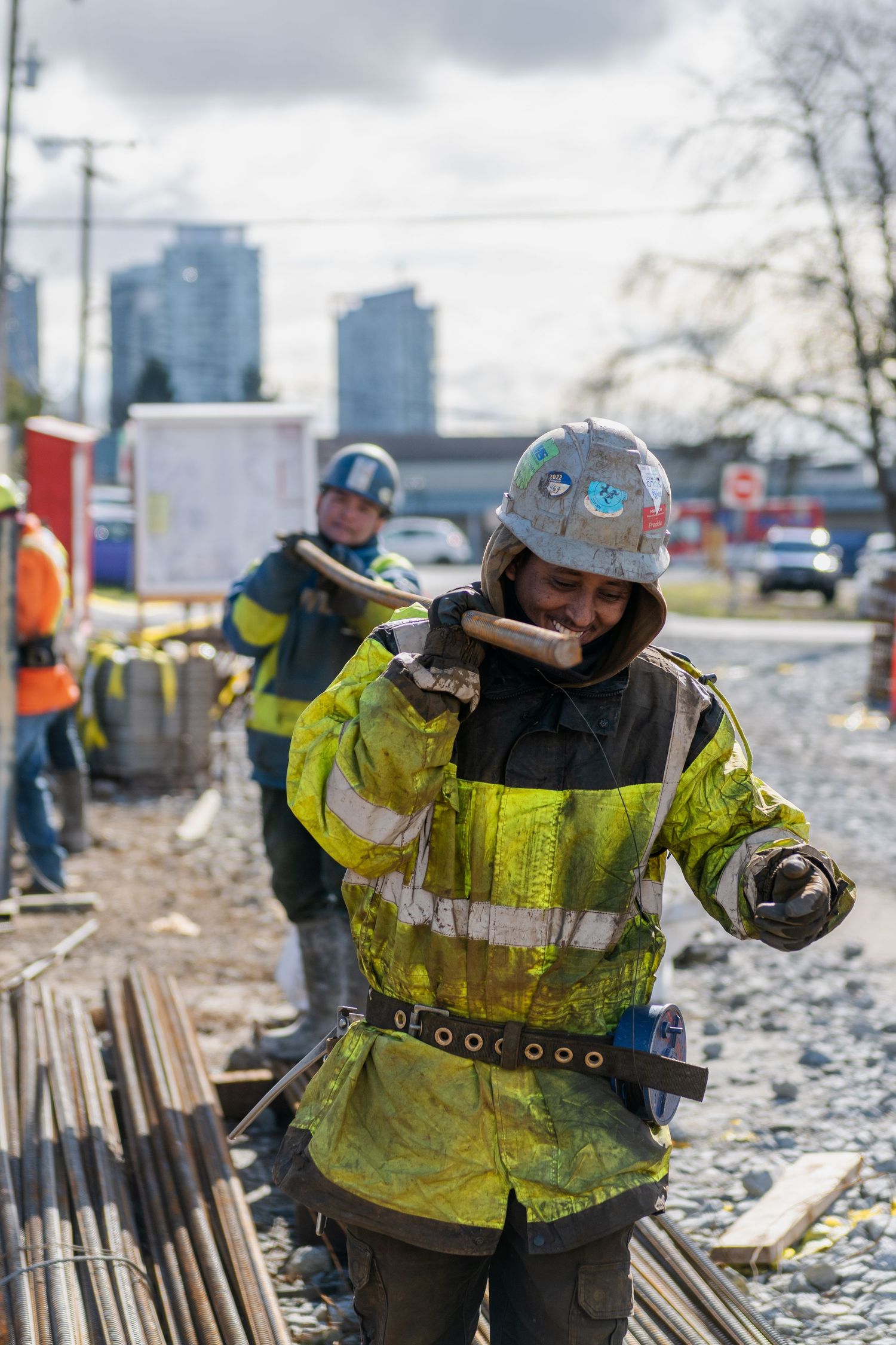 Construction worker in yellow high-visibility jacket and hard hat carrying a sledgehammer at an urban job site.