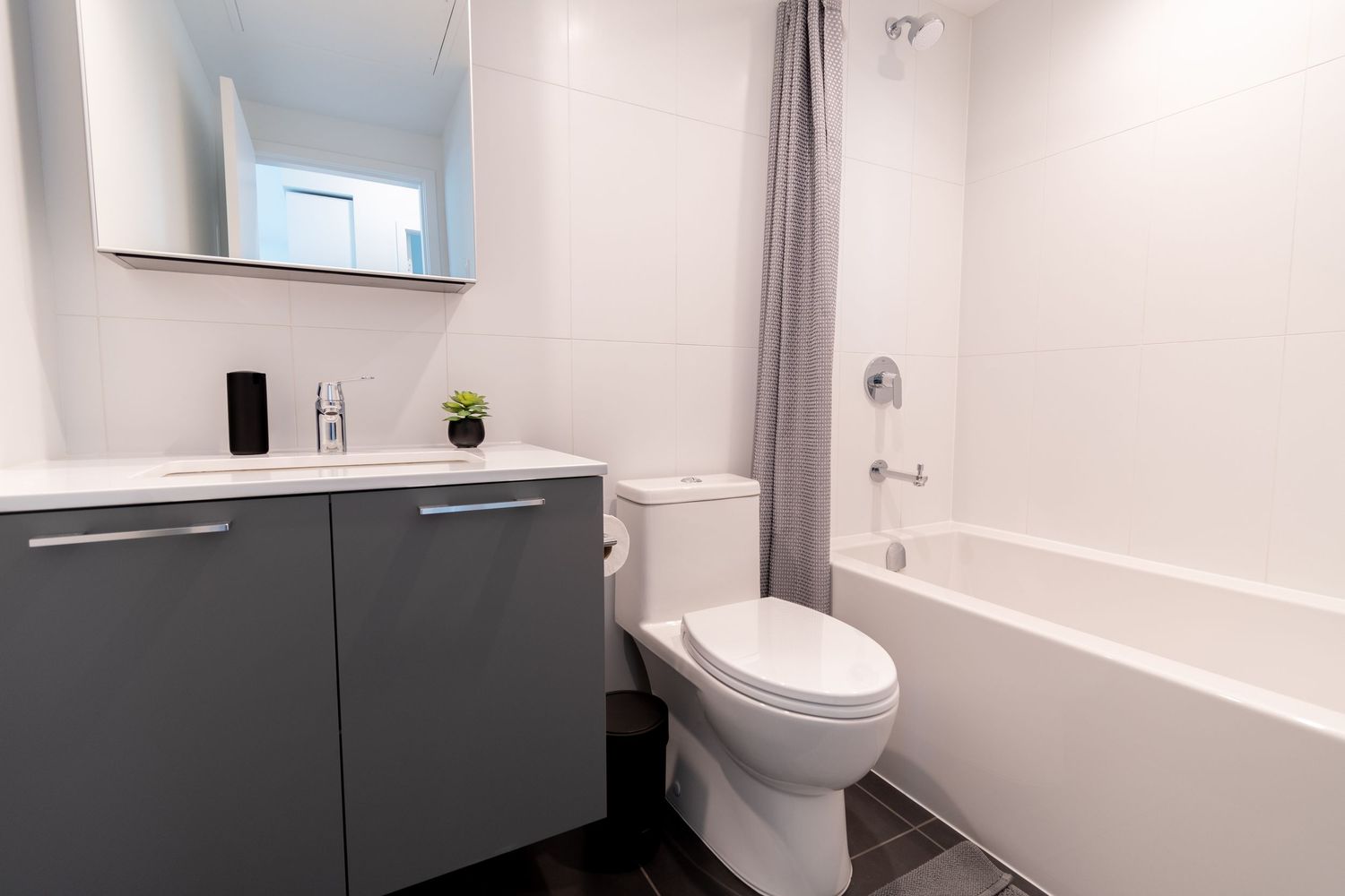 Clean modern bathroom with gray vanity, white subway tiles, toilet, and shower-tub combo with curtain.