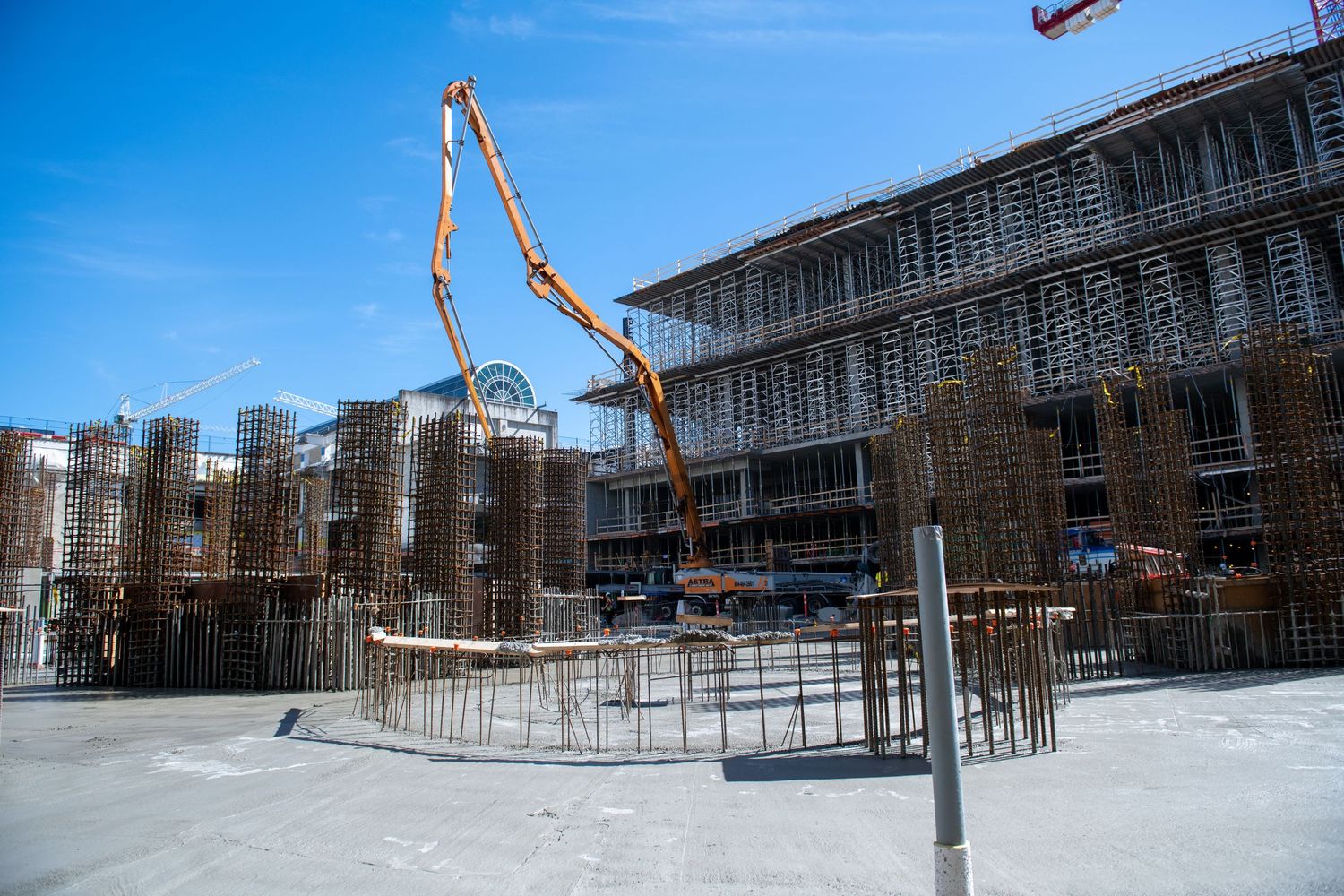 Construction site with rebar columns and an orange concrete pump boom under a clear blue sky.
