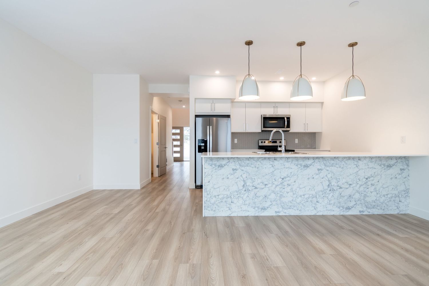 Modern open-plan kitchen with marble island, white cabinets, pendant lights and light wood floors.