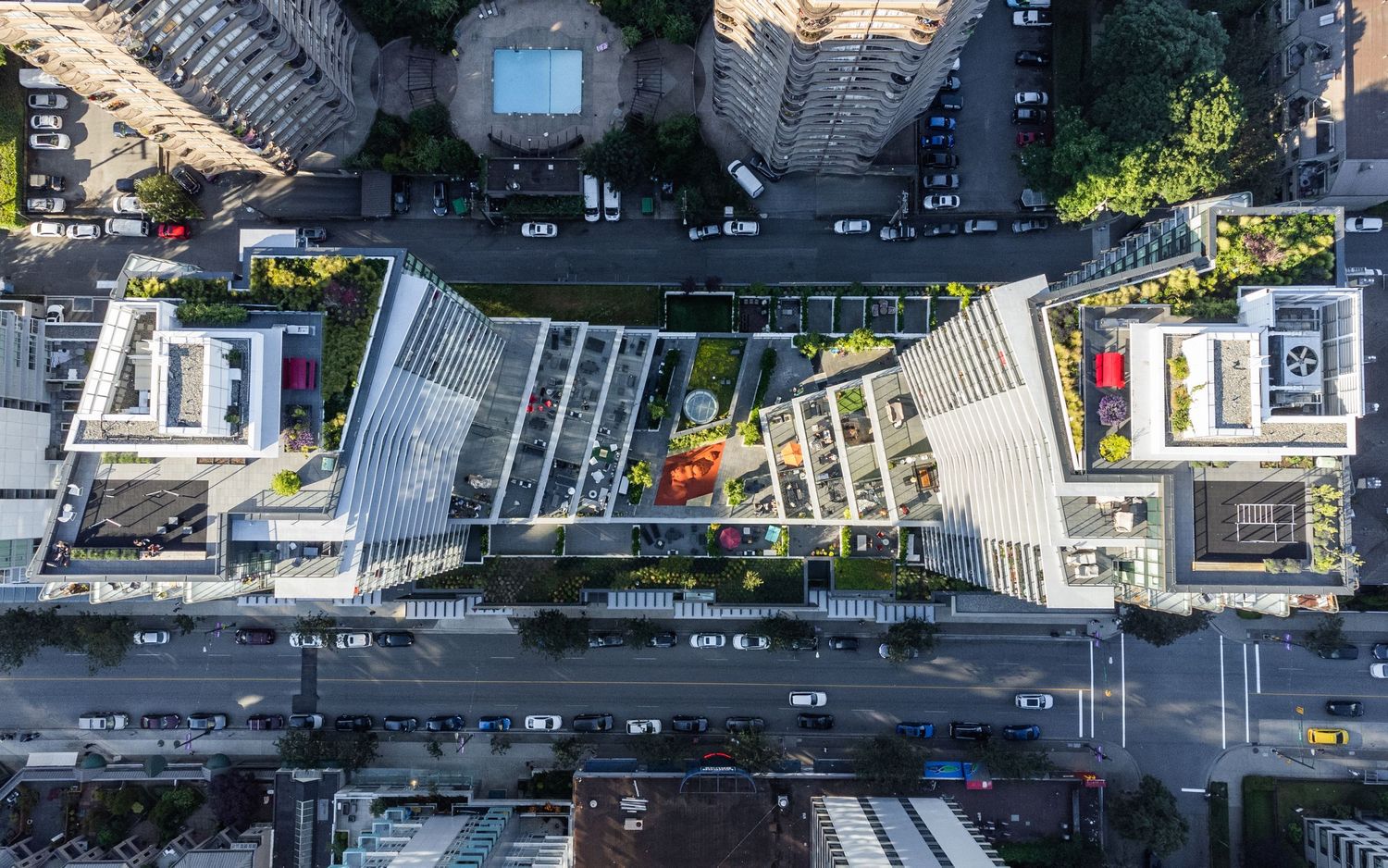 Aerial top-down view of modern urban city block with green rooftop gardens and busy intersection.