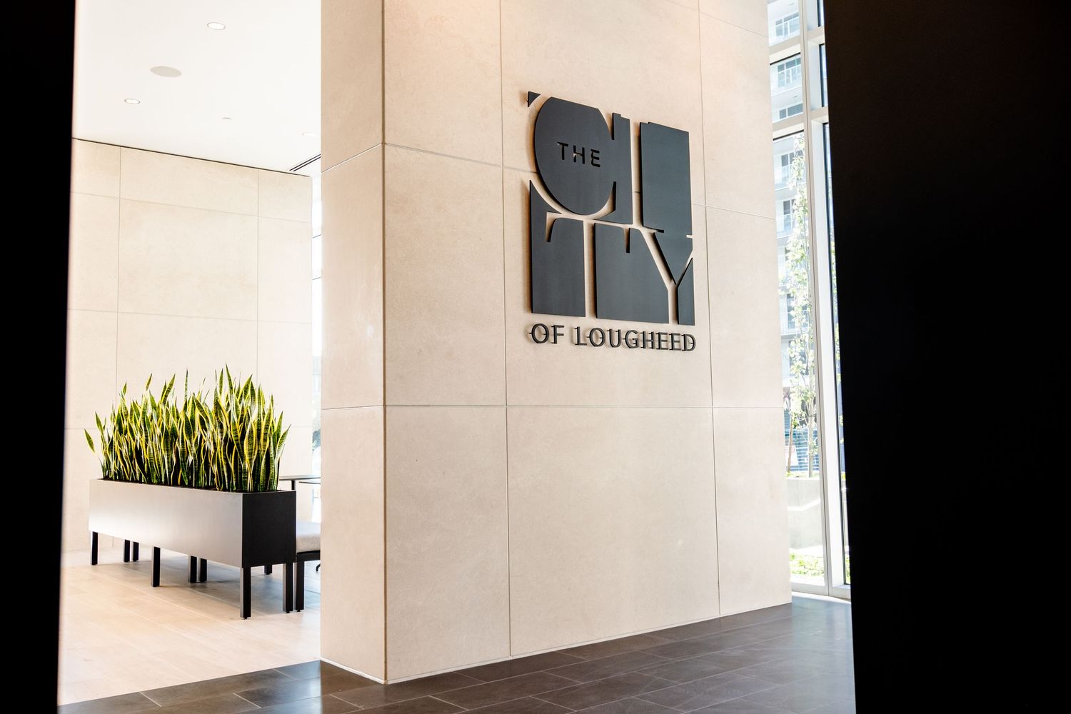 Modern lobby entrance featuring The City of Lougheed signage with elegant stone walls and decor.
