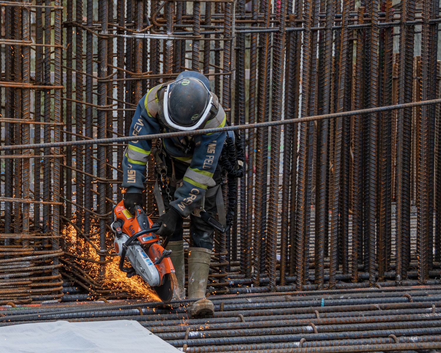 Construction worker cutting rebar with an angle grinder, sending sparks flying at a building site.