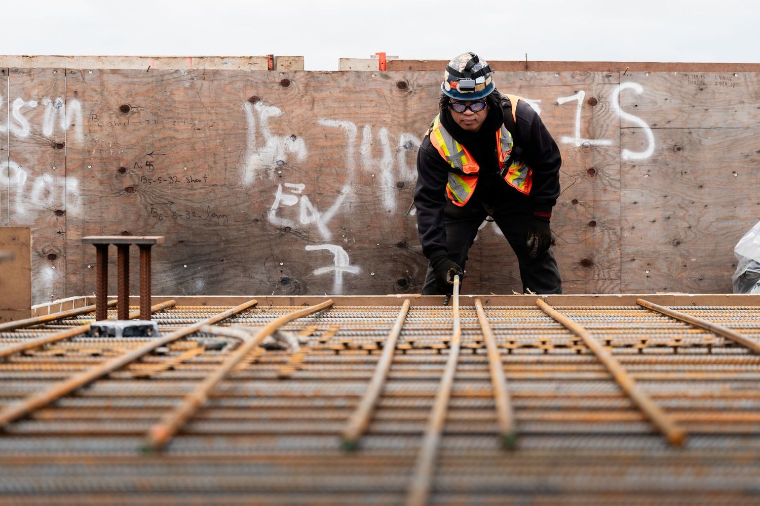 Construction worker in safety gear tying rebar on a concrete formwork at a high-rise building site.