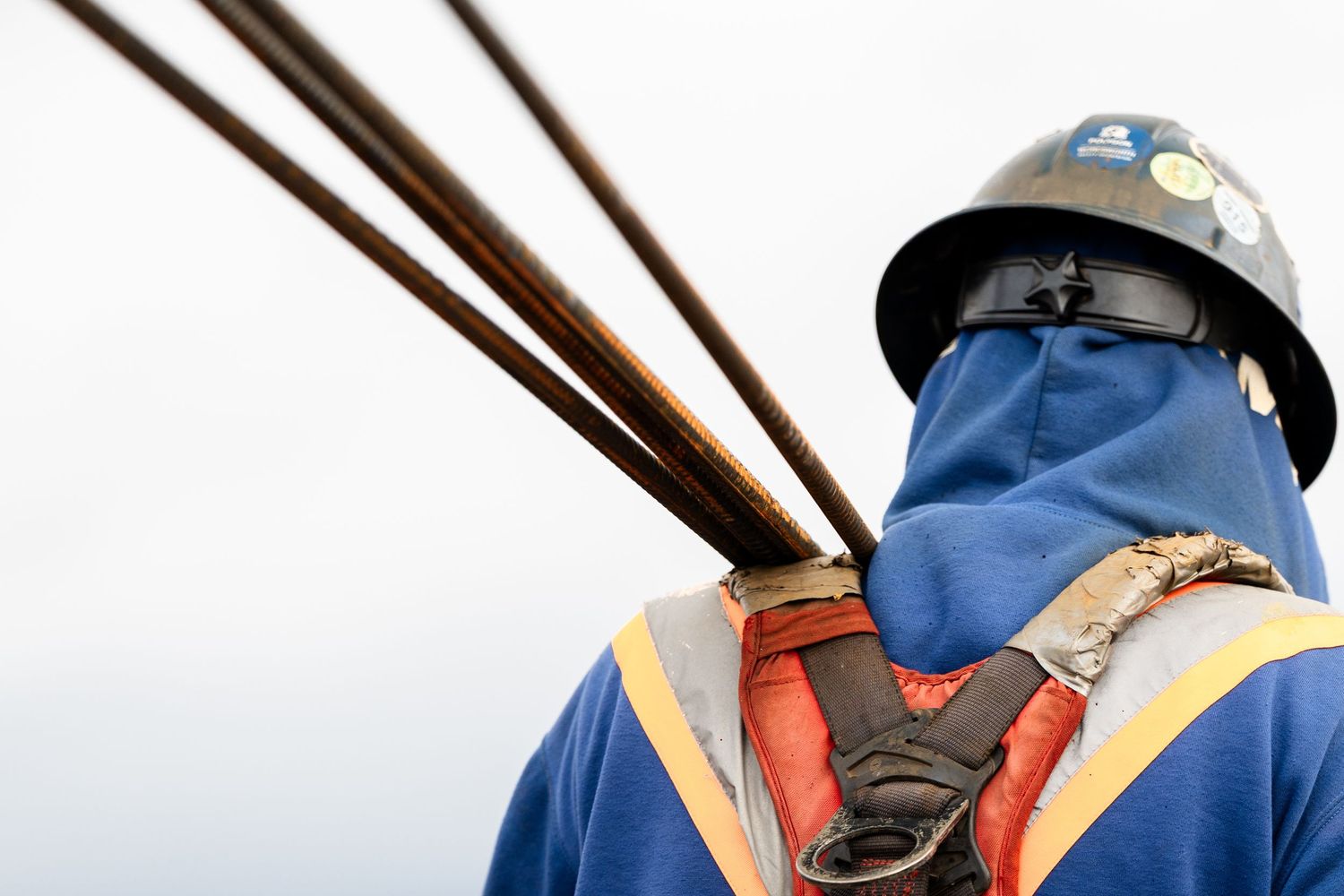 Construction worker in hard hat and safety vest carrying steel rebar on a high-rise building site.