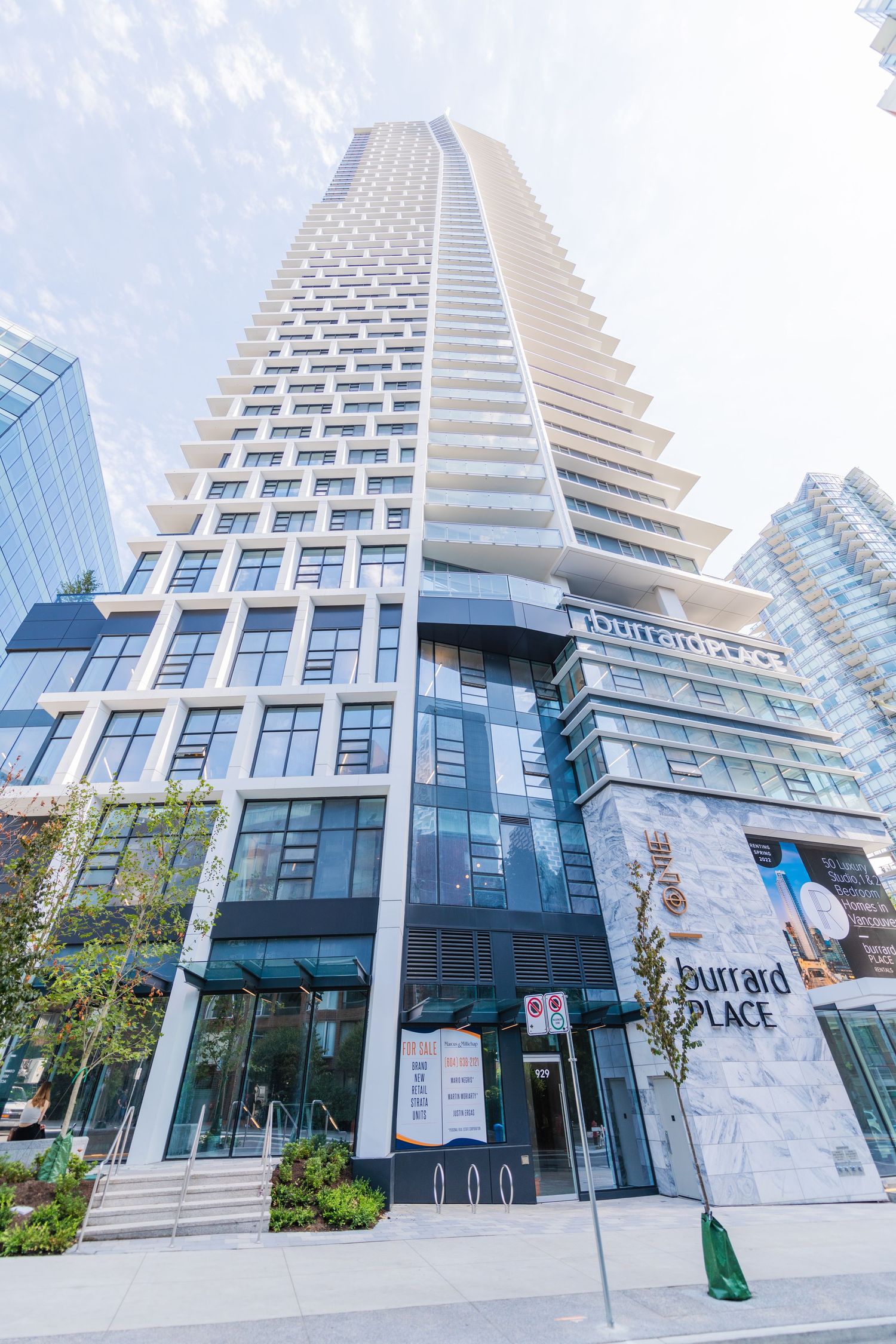 Street-level view looking up at Burrard Place luxury high-rise tower with glass retail podium entrance.