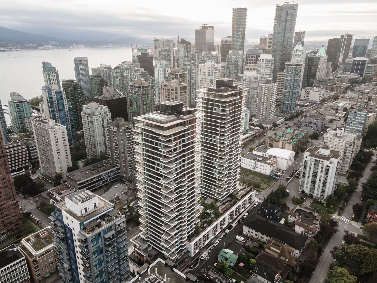Aerial view of dense downtown Vancouver skyline with waterfront and residential towers.