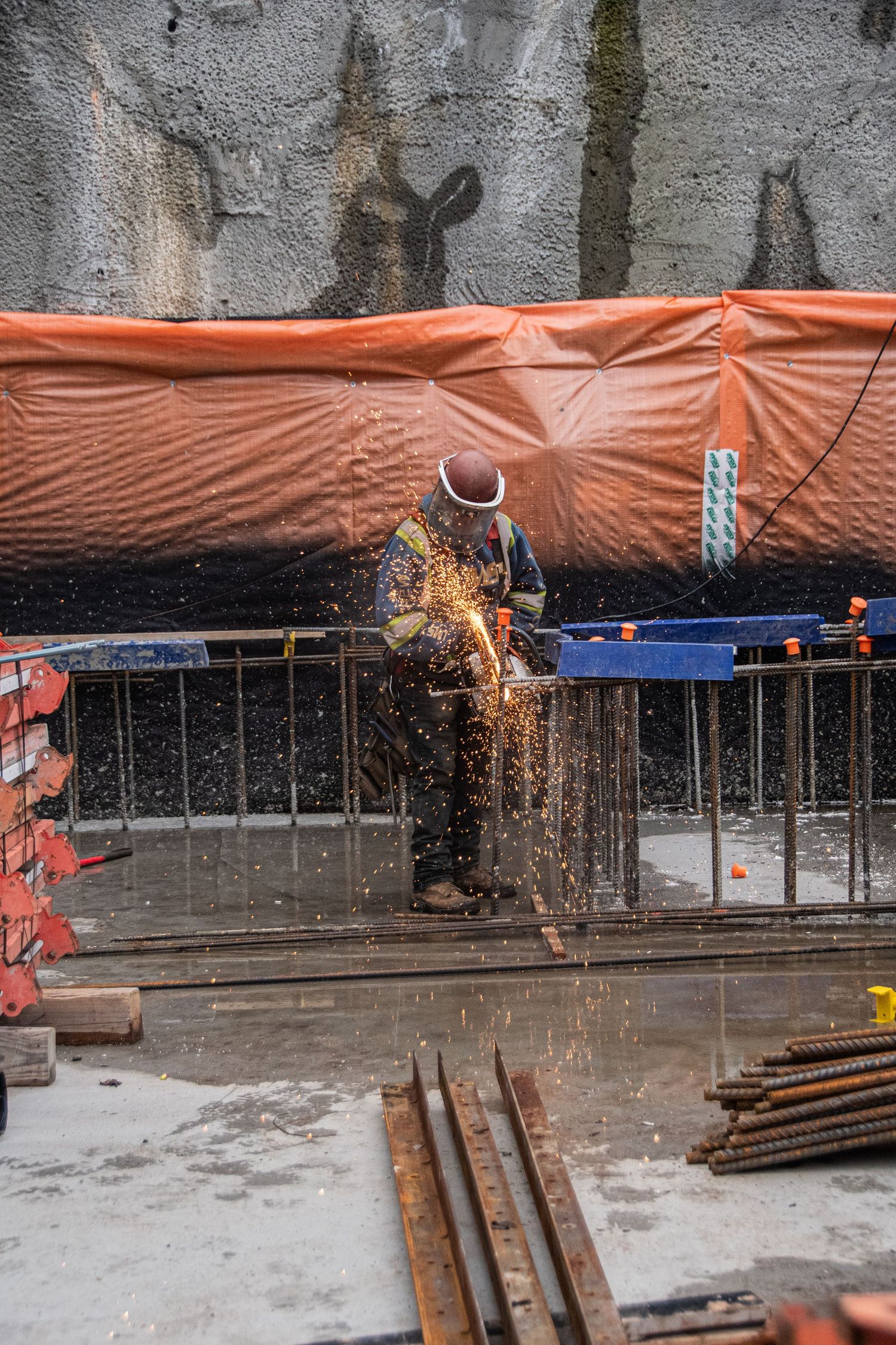 A welder in safety gear creates bright sparks while working on steel rebar at a construction site.