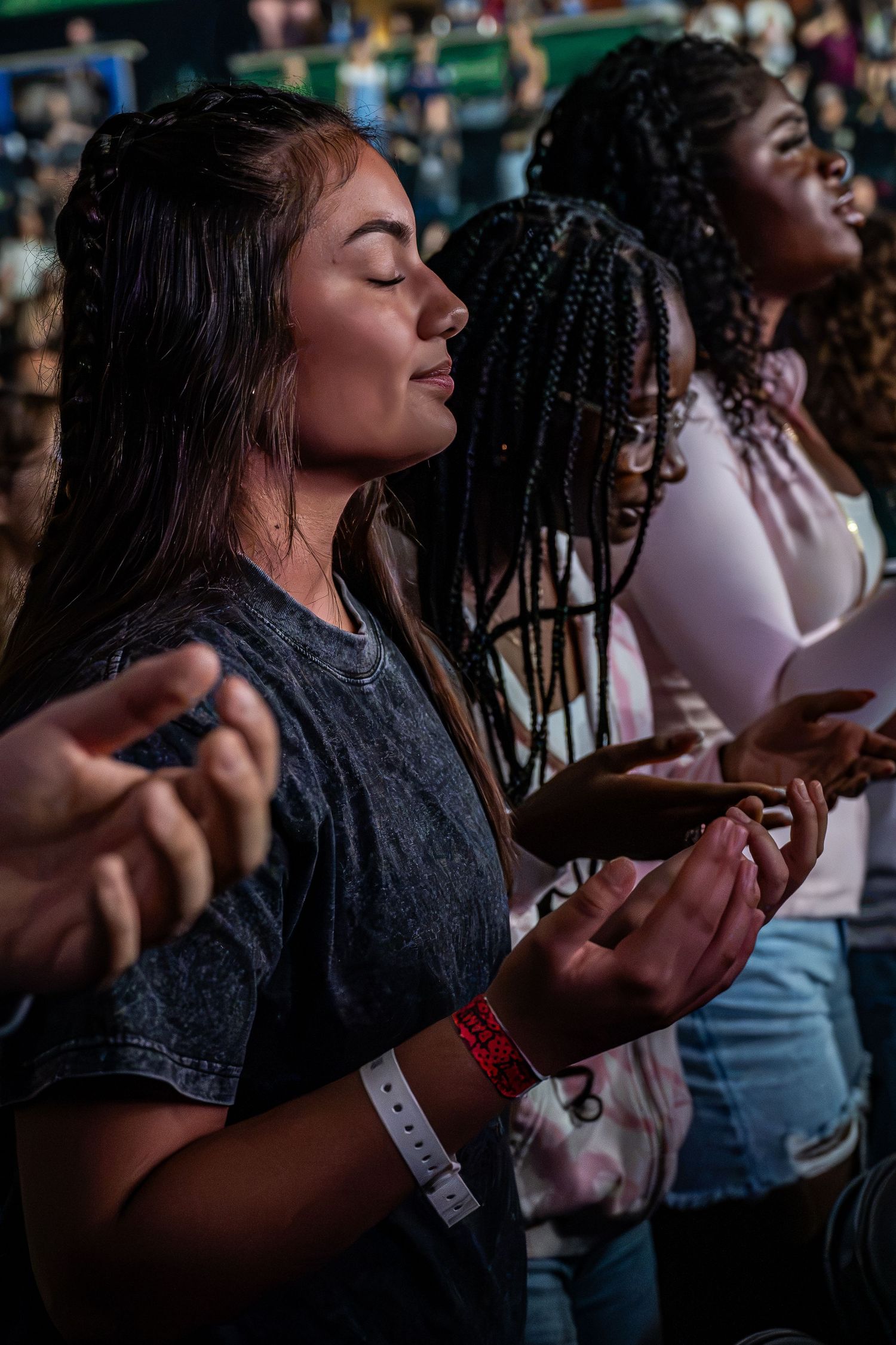 Two young women with eyes closed in peaceful prayer and worship at a Christian event.