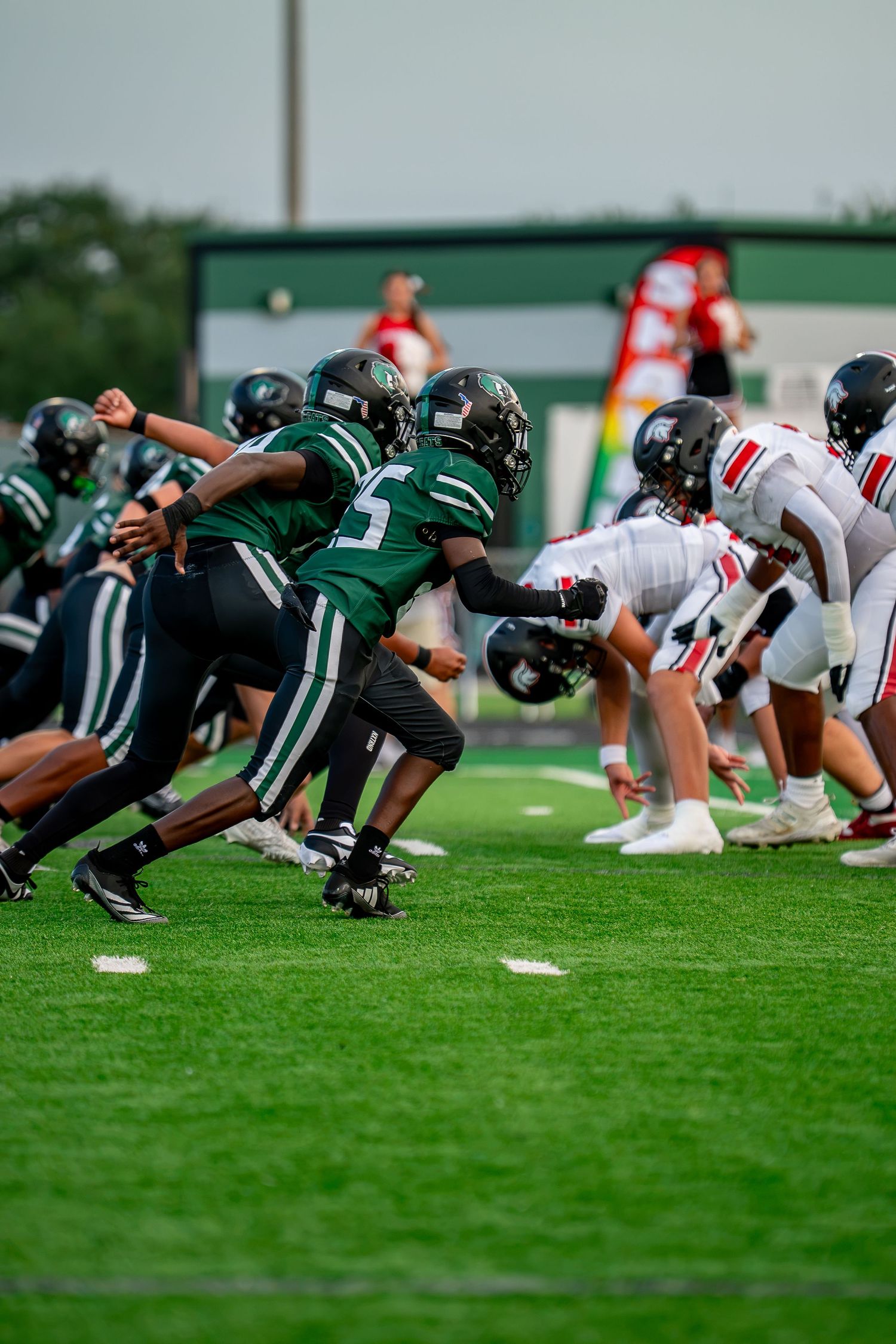 Green and white high school football team lines up against red and white opponents at scrimmage.