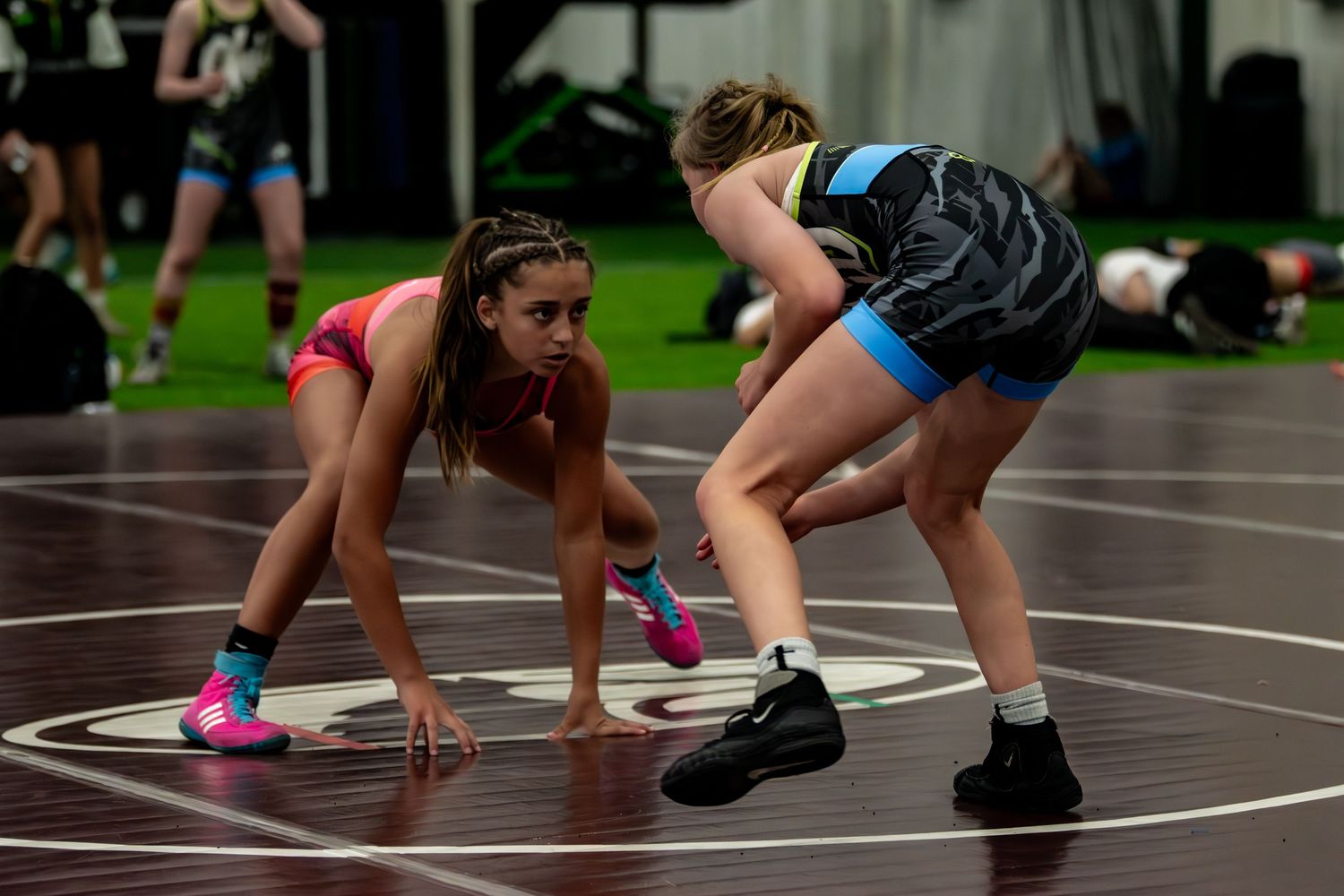 Two female wrestlers in colorful singlets in a crouched stance during practice match.