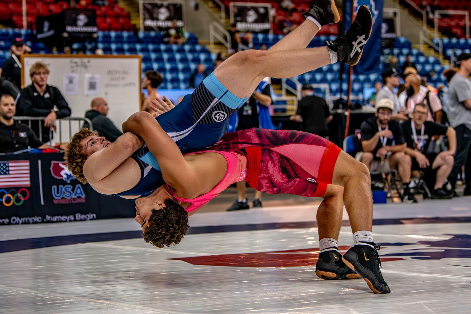 Wrestler executing a dramatic throw during USA Olympic wrestling competition on blue mat.