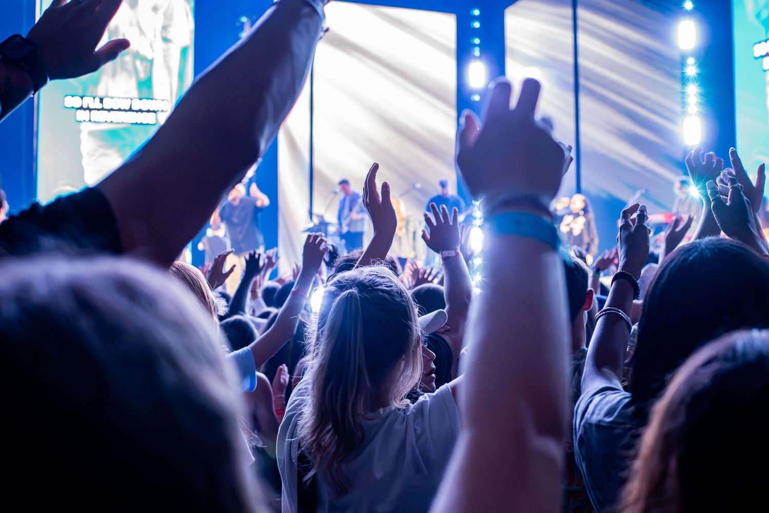 Crowd of young people raising hands in worship at a large Christian music concert.