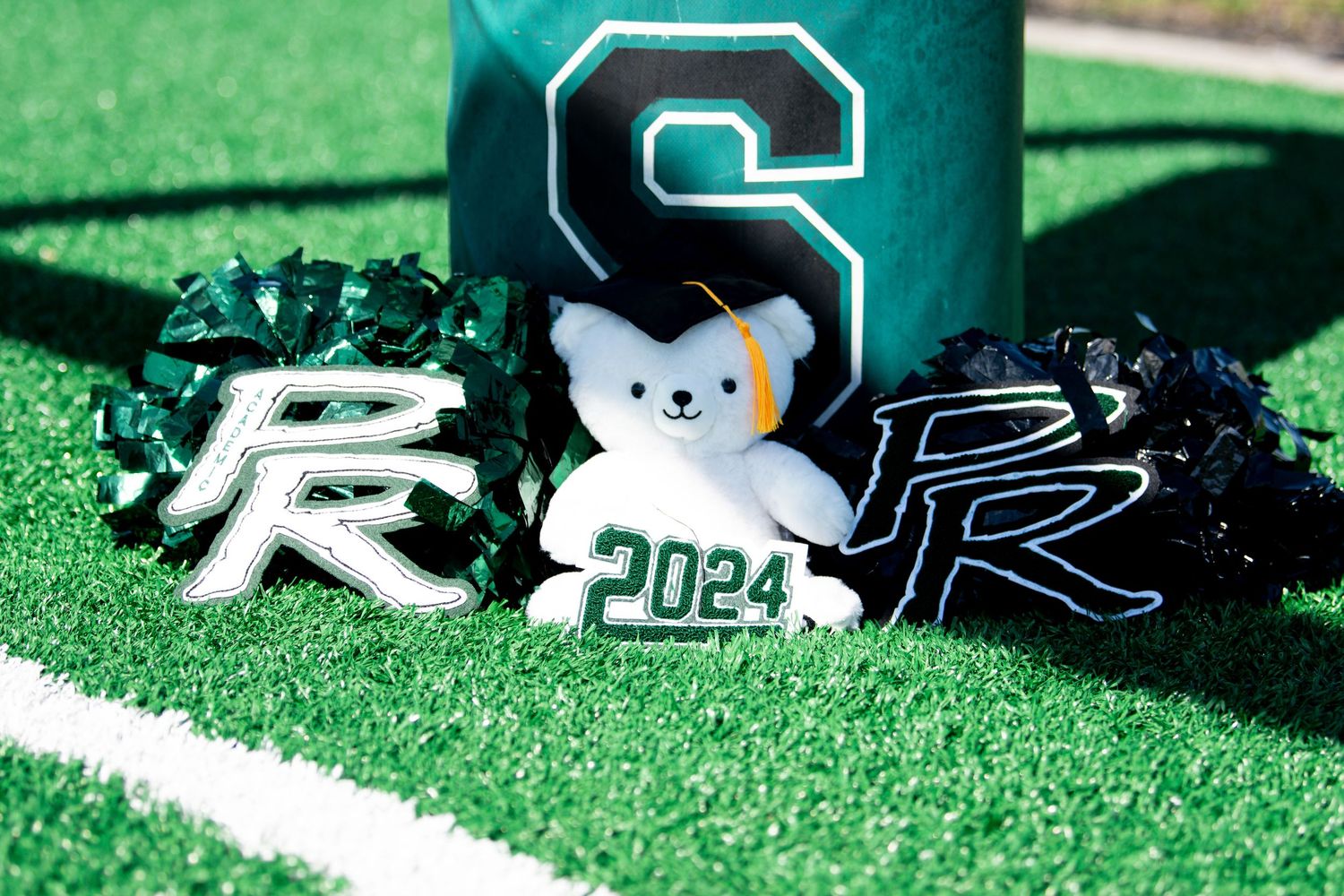 Senior 2024 graduation items including teddy bear, pom poms near green S field marker.