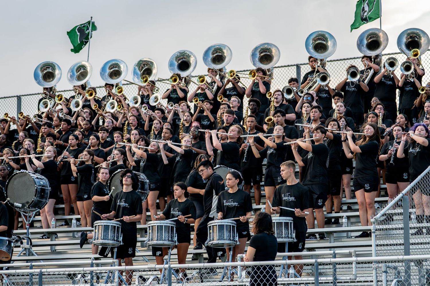 High school marching band performs in stadium bleachers during a football game.