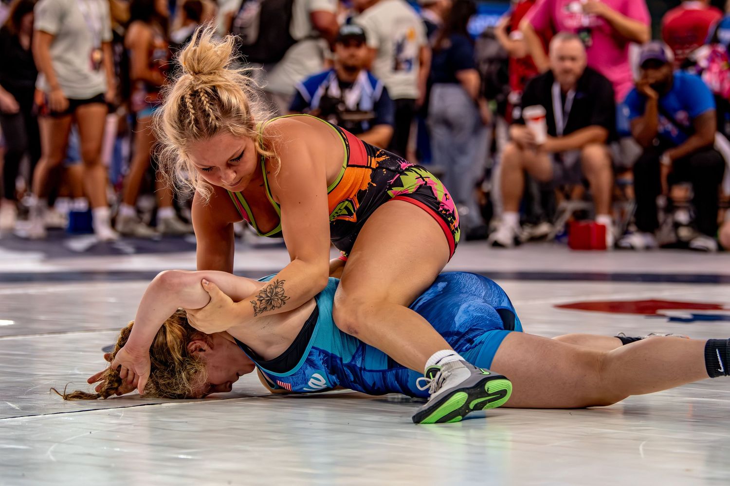 Two female wrestlers competing on mat, one in orange pinning opponent at tournament.