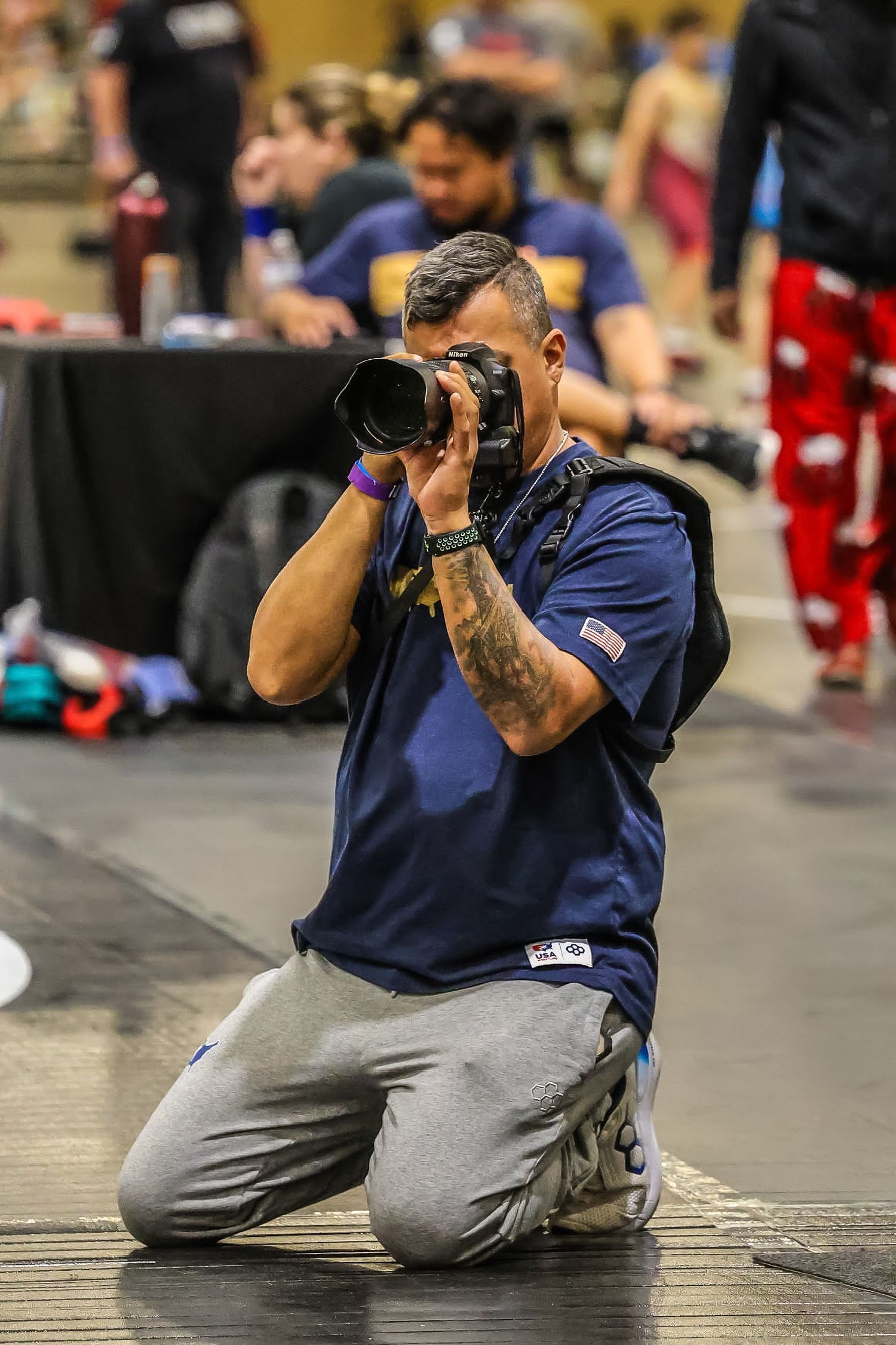 Photographer kneeling on floor capturing shots with professional camera at indoor event.