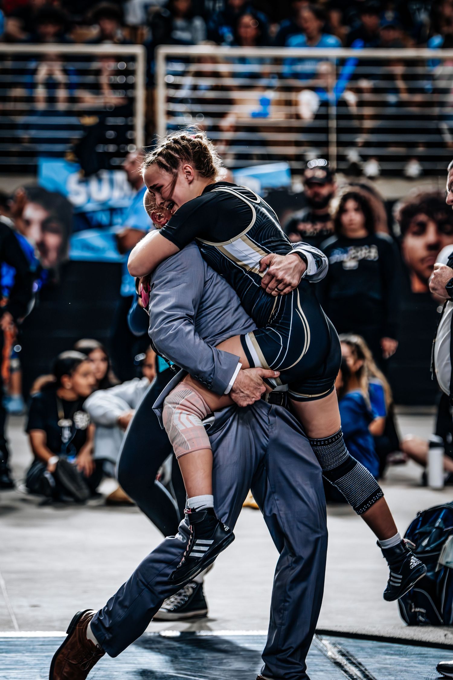 Female wrestler lifts opponent during intense match at crowded indoor wrestling tournament competition.