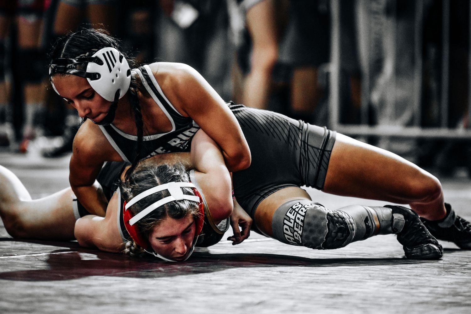Two male wrestlers grapple on the mat during an intense high school wrestling match.