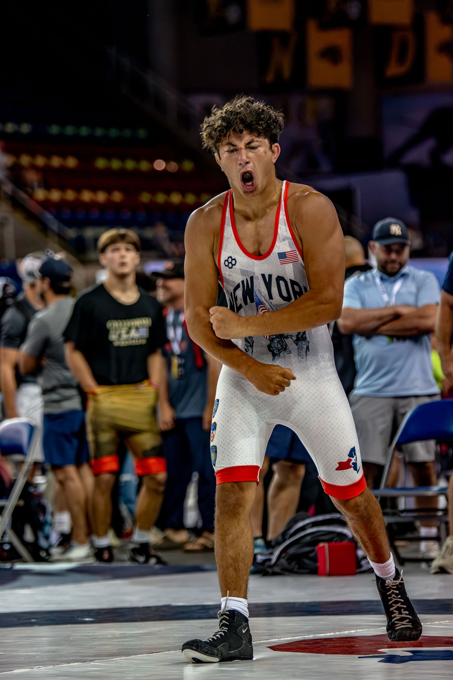 Excited young male wrestler in New York white singlet celebrates victory with a fist pump at a wrestling tournament.