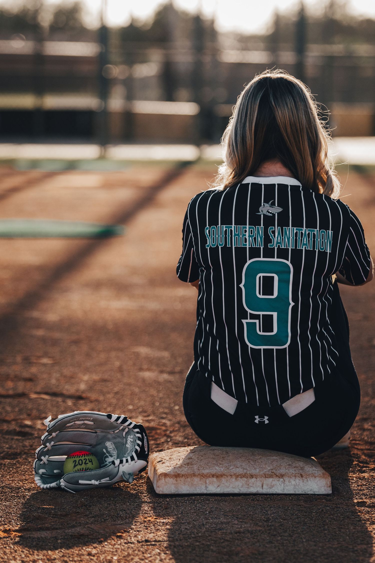 Softball player in Southern Sandstorm jersey number 9 sitting on base with glove nearby.