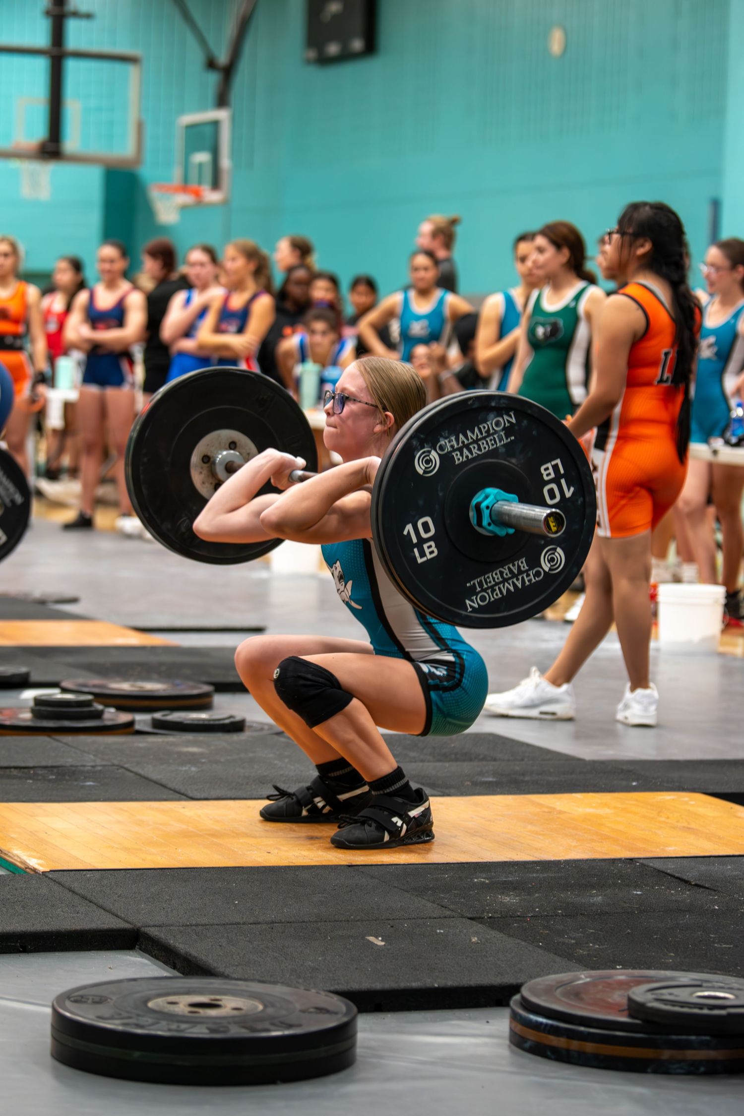 Young female weightlifter performing a clean squat with a loaded barbell at an indoor youth weightlifting competition.