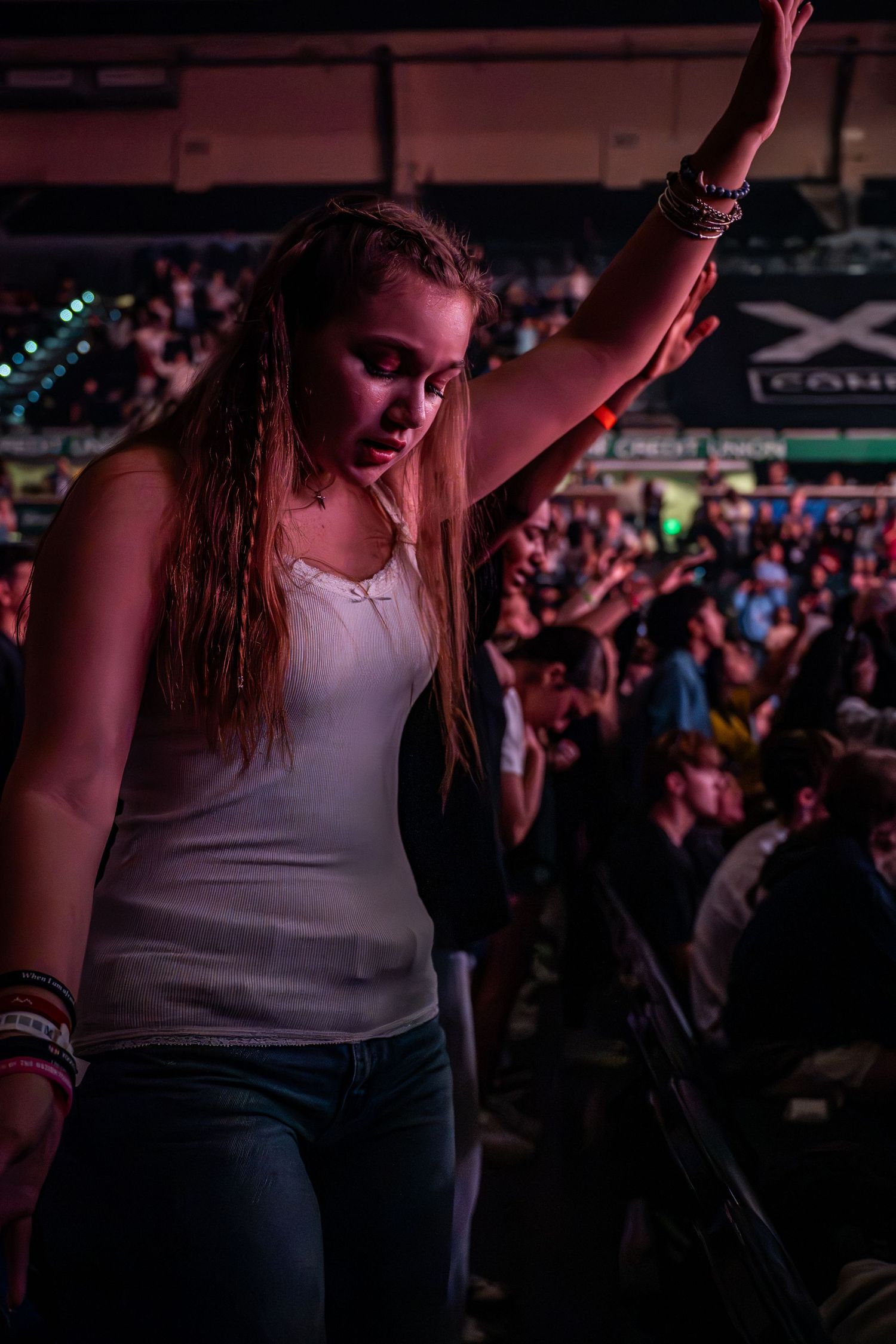 Teenage girl with long hair raises hand in praise at an indoor worship concert event.