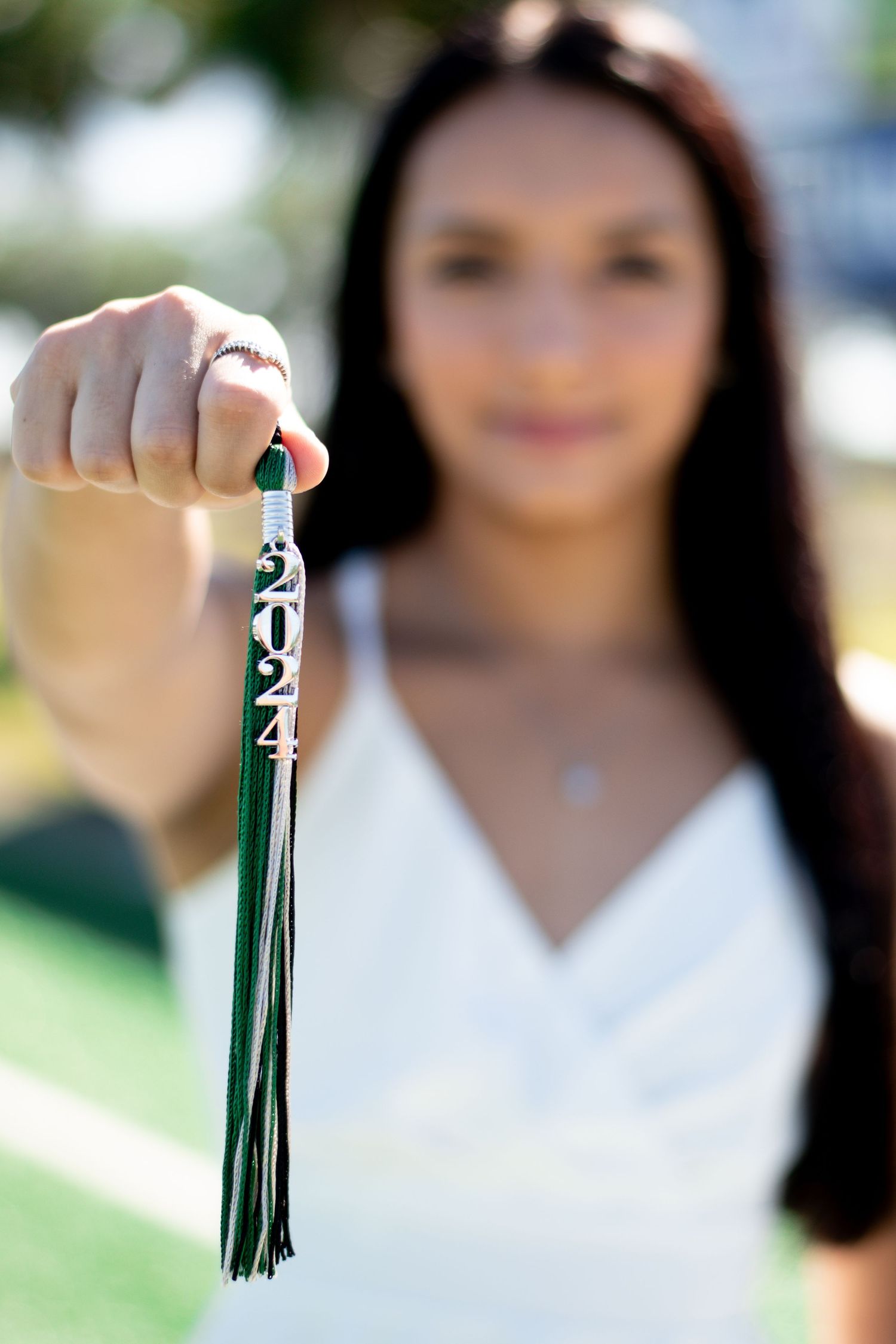 Graduate holding green 2024 tassel close to camera during outdoor senior portrait session.