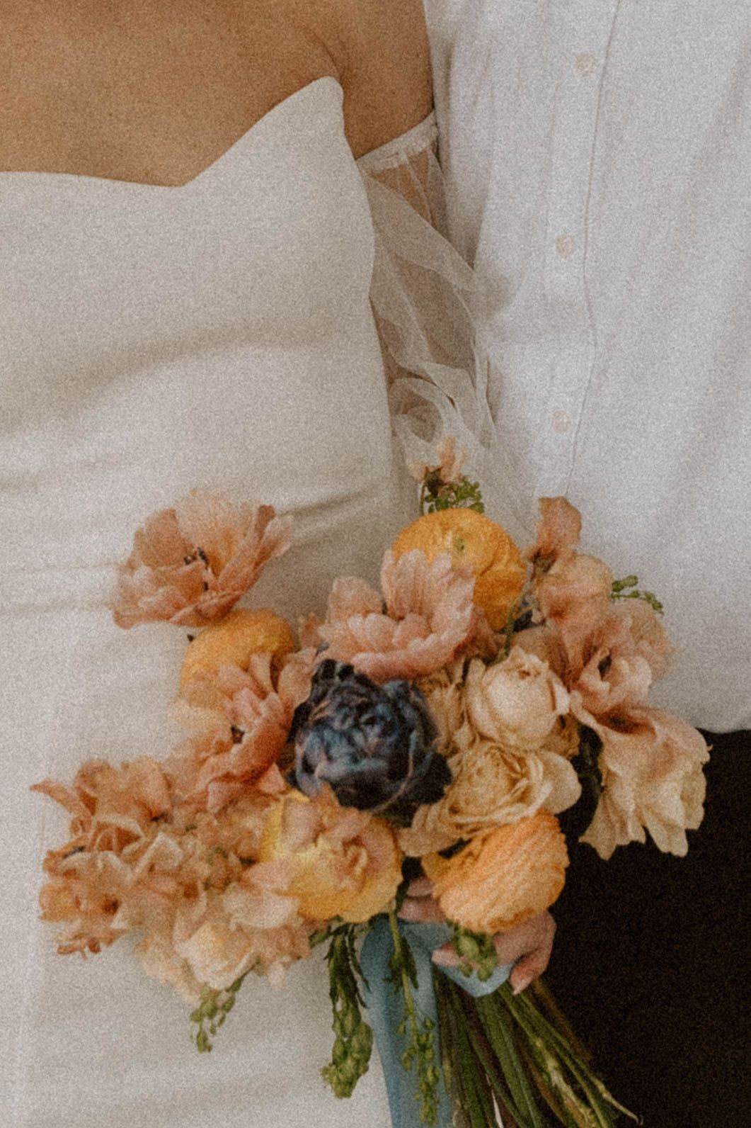 Delicate peach and cream floral bouquet resting against white pillows and linens.