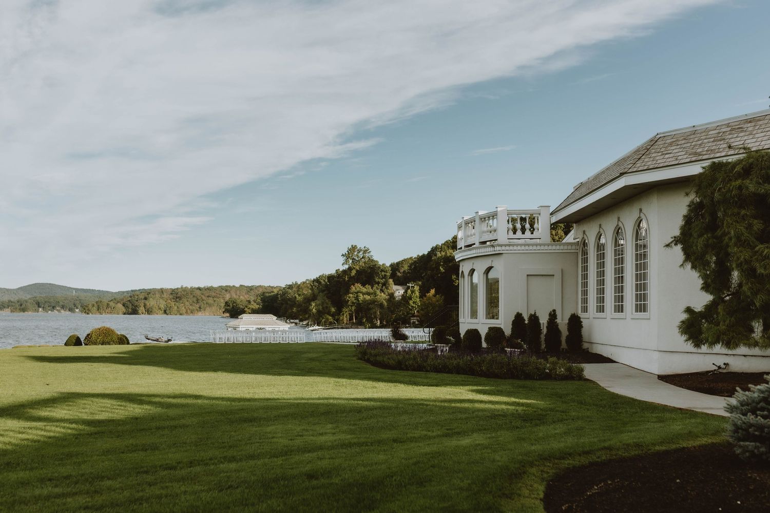 Luxury waterfront mansion with manicured lawn overlooking scenic coastal bay on a calm sunny day.