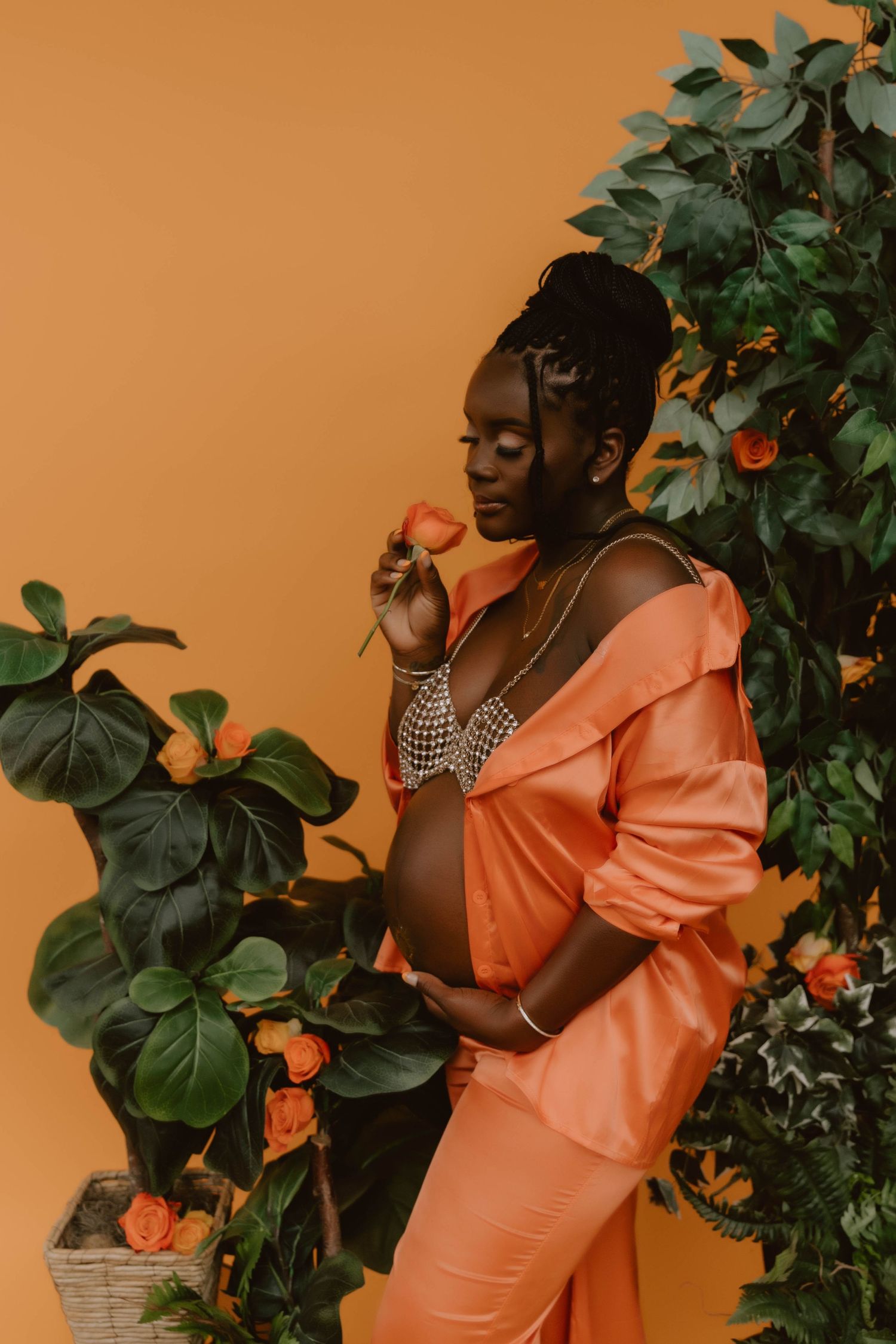 Pregnant Mama in coral orange outfit poses elegantly with oranges and tropical foliage against peachy backdrop.