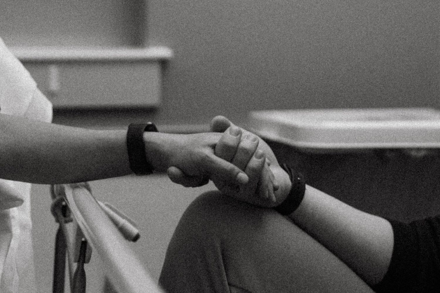 A black and white image shows two hands clasped together in an emotional gesture of comfort and support.
