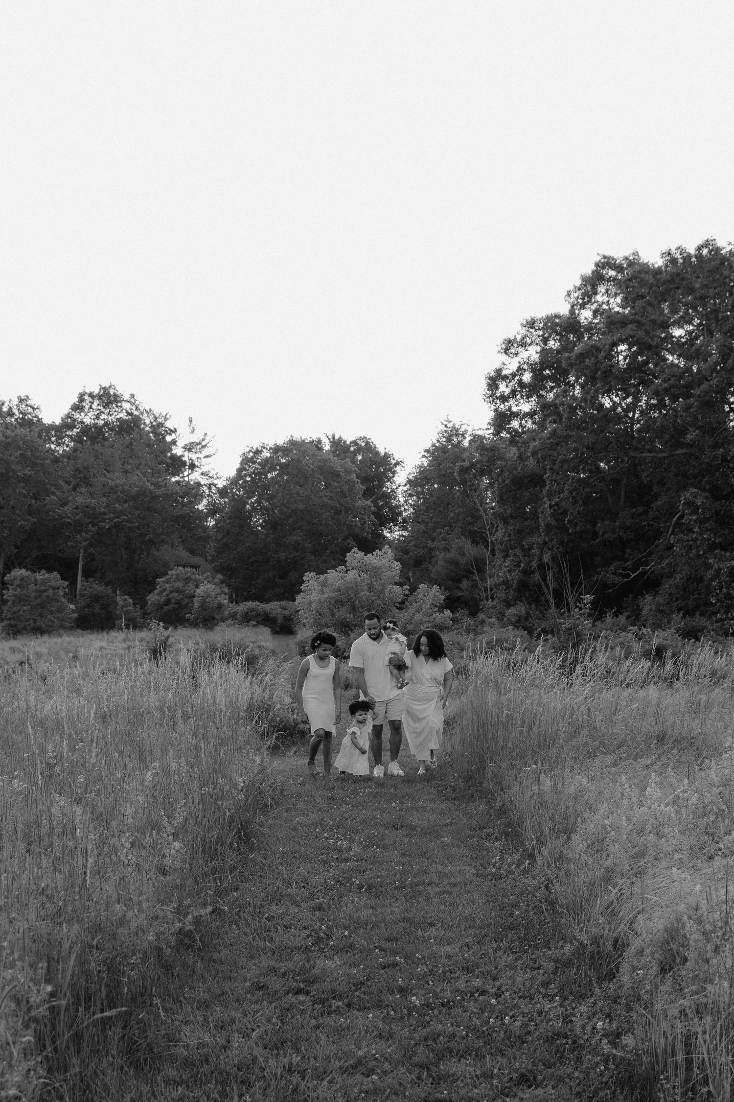 A black and white photo showing three people walking together through a rustic meadow path.