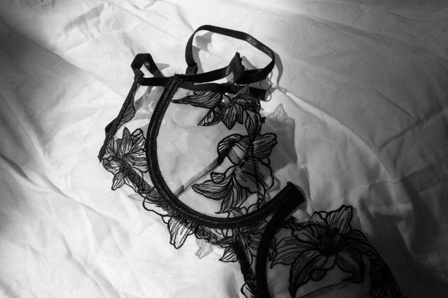 Black and white photograph of delicate floral lace trim with curved patterns on white fabric.