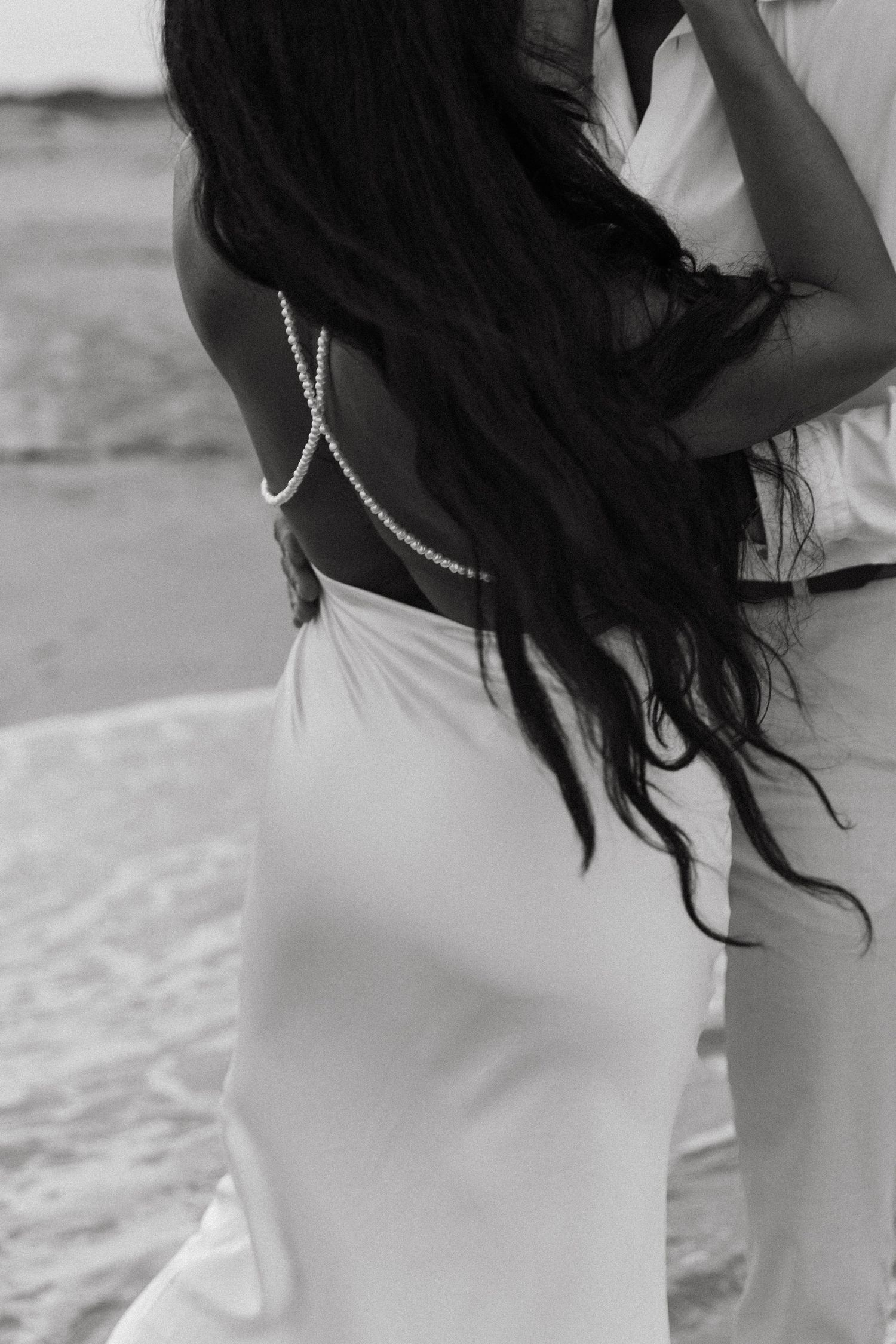 Black and white photo of dark wavy hair blown by wind against a white background, showing a graceful movement pattern.