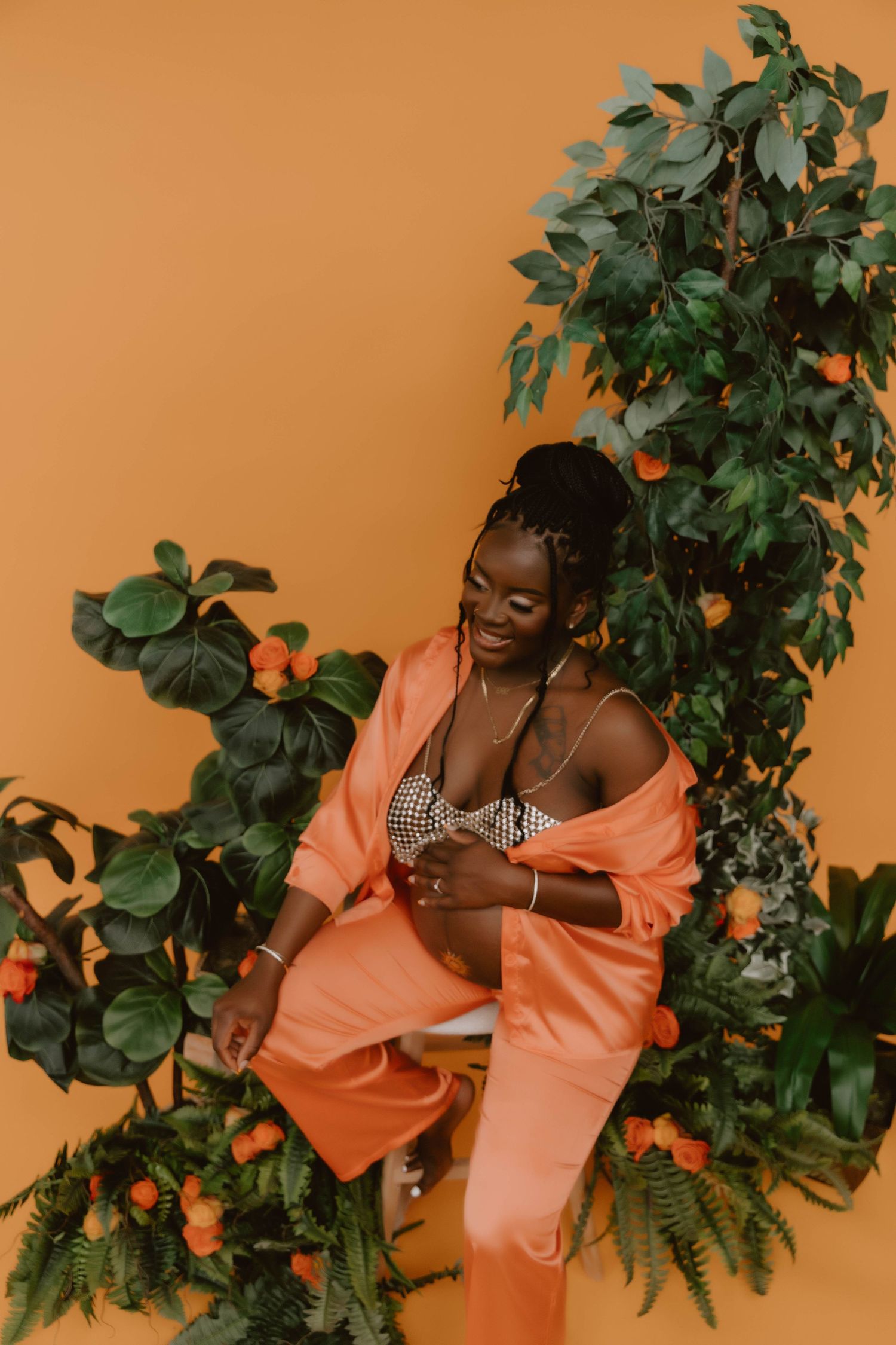 Artistic portrait with model in peach ensemble surrounded by citrus trees against orange wall.
