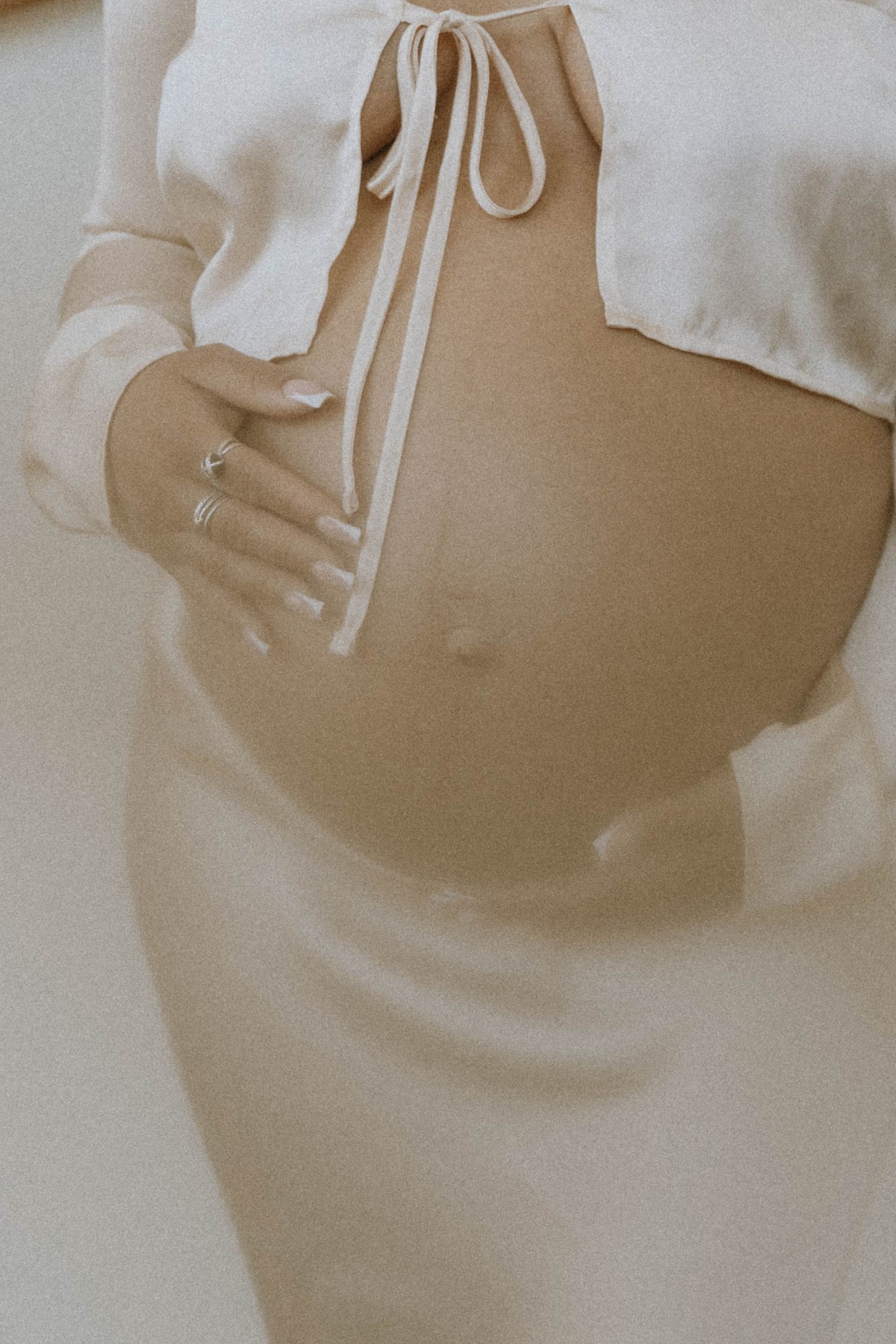 Close-up of a person wearing cream-colored clothing with drawstring detail and ring visible.