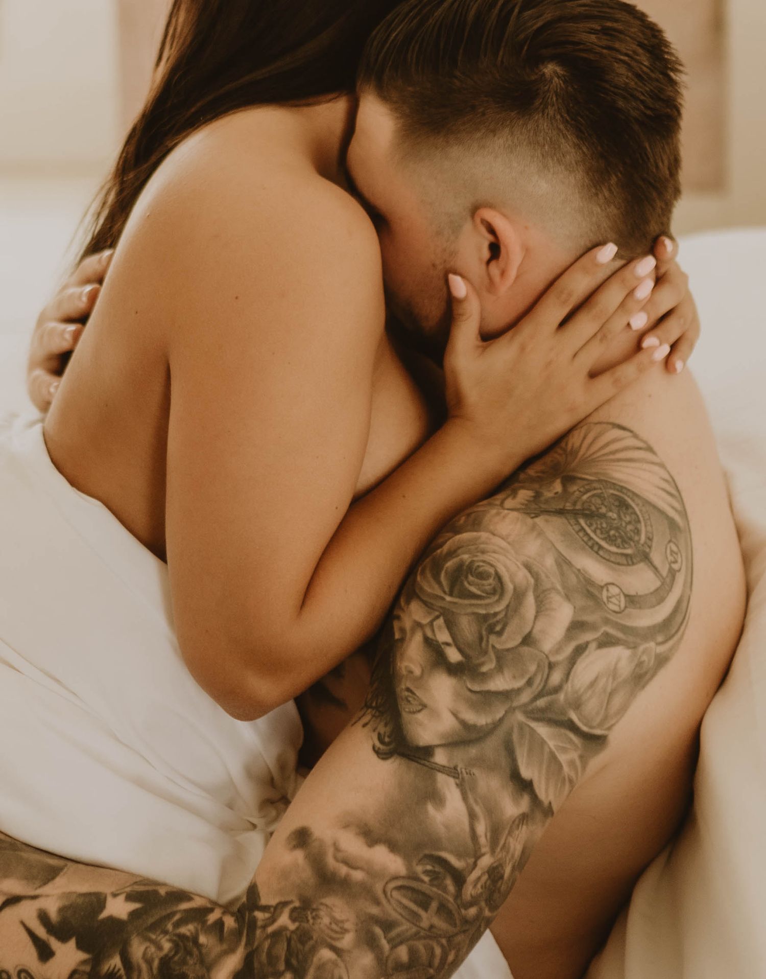 Intimate couple embracing with detailed floral tattoo sleeve visible in warm lighting.