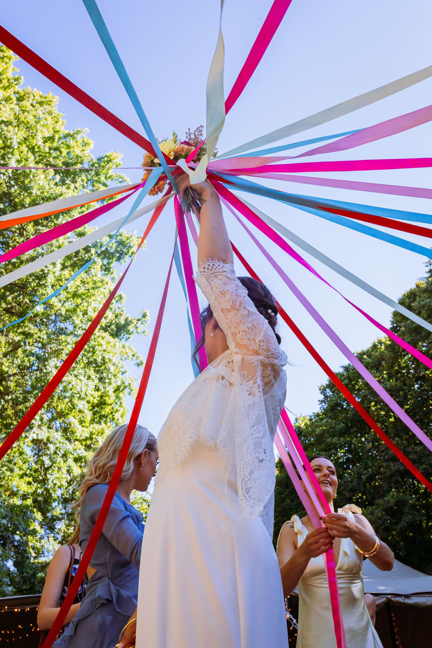 Colorful ribbons in pink, blue, and red create a maypole-style decoration against a sunny outdoor backdrop.