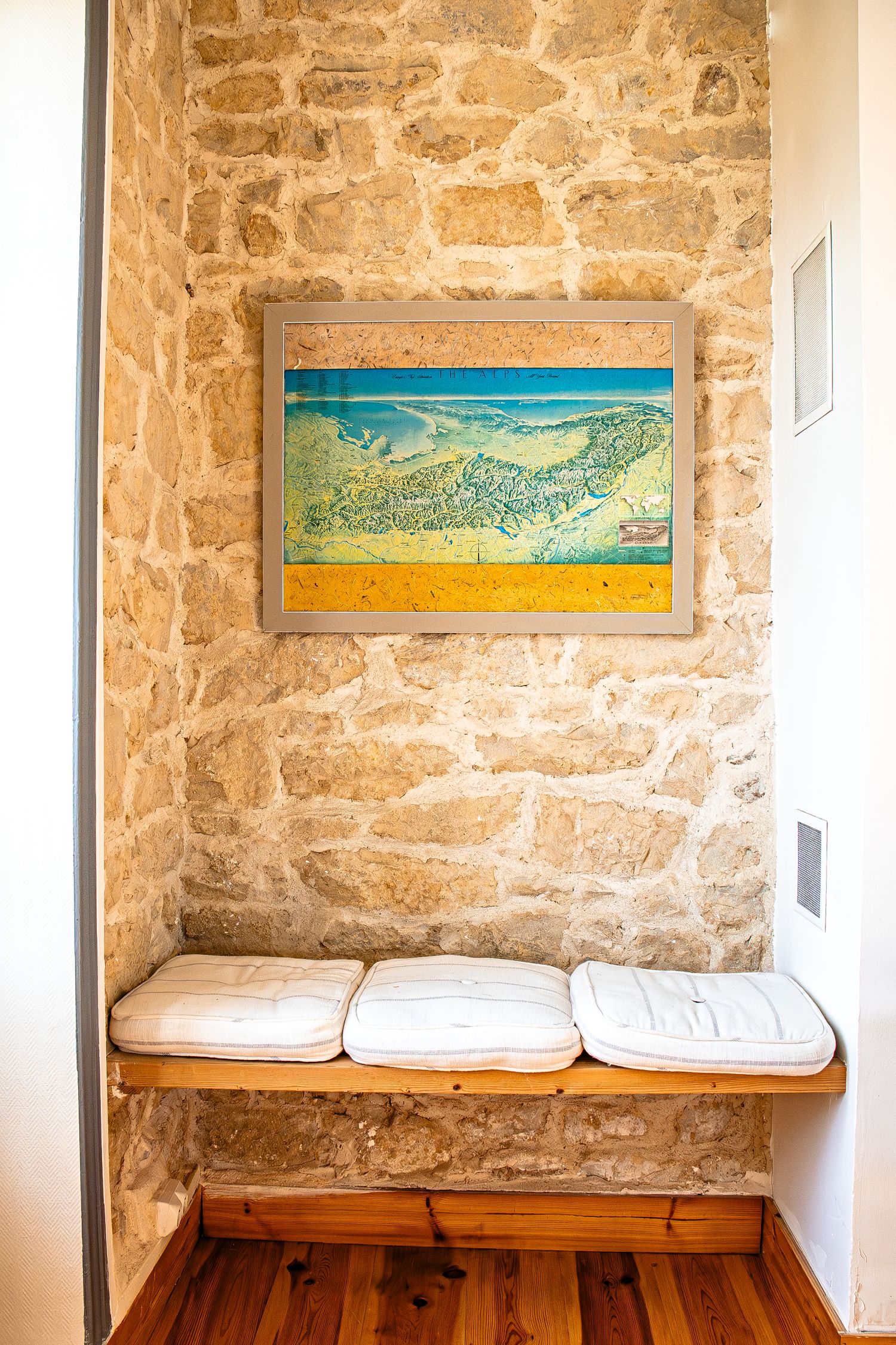 Stone wall interior with wooden bench seating and colorful landscape artwork mounted on rustic walls.