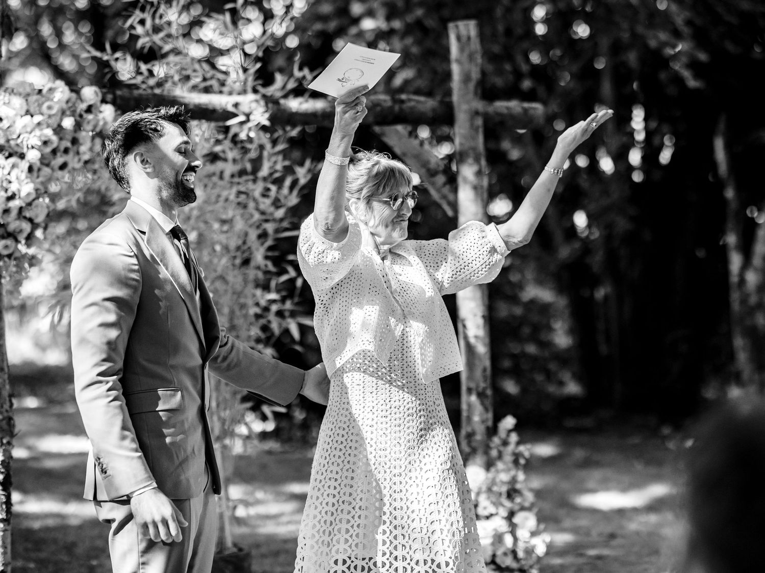 Vintage black and white photo of people in 1920s clothing waving joyfully outdoors in a garden setting.