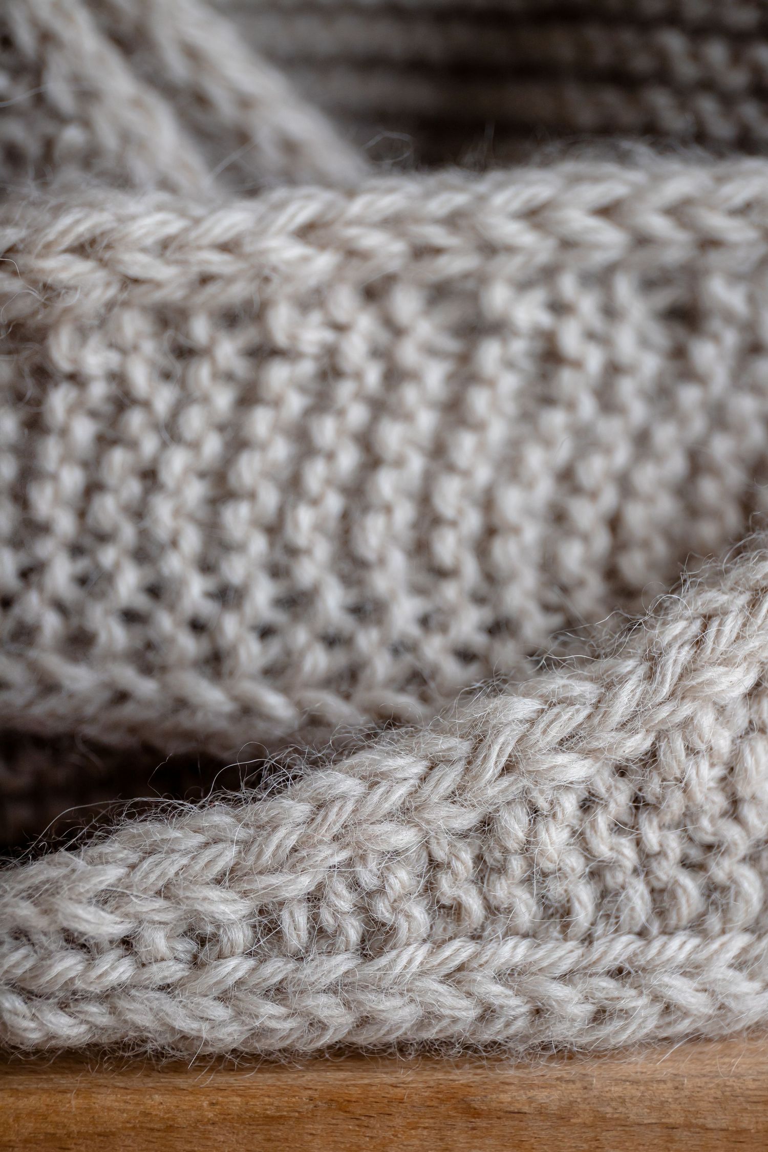 Close-up detail of beige knitted wool texture showing intricate stitch pattern.