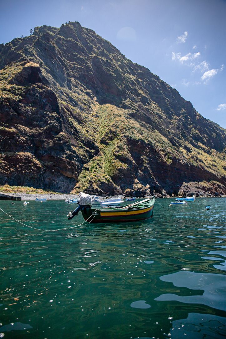 Boats anchored near dramatic coastal cliffs with emerald green waters.