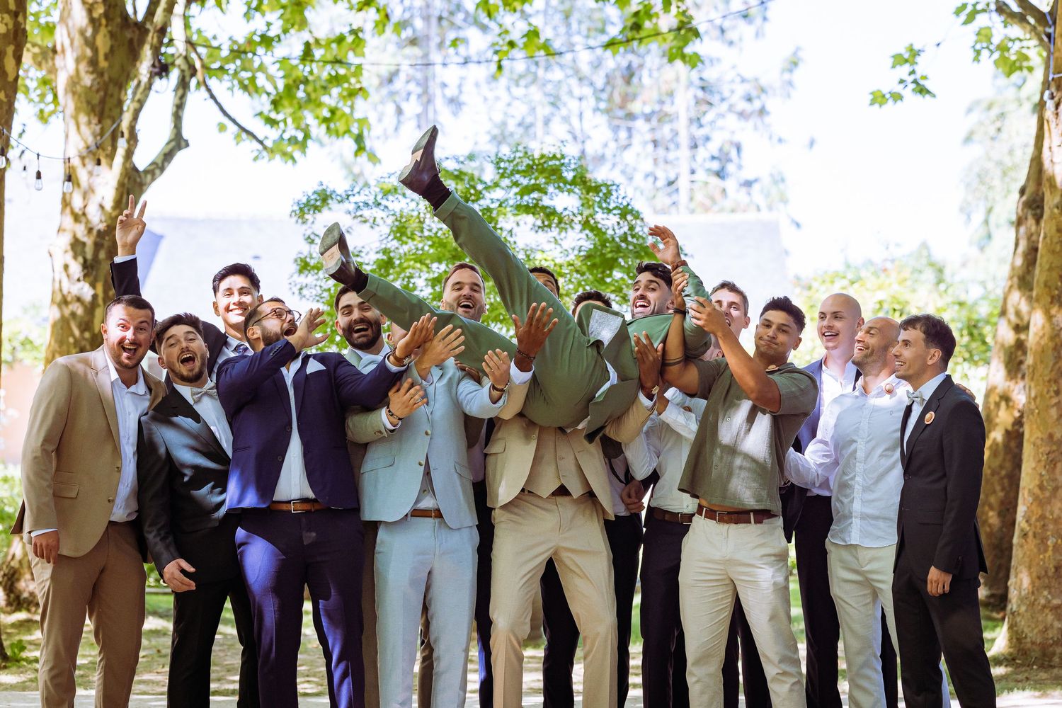 Wedding party gathers under trees for outdoor celebration in formal attire.