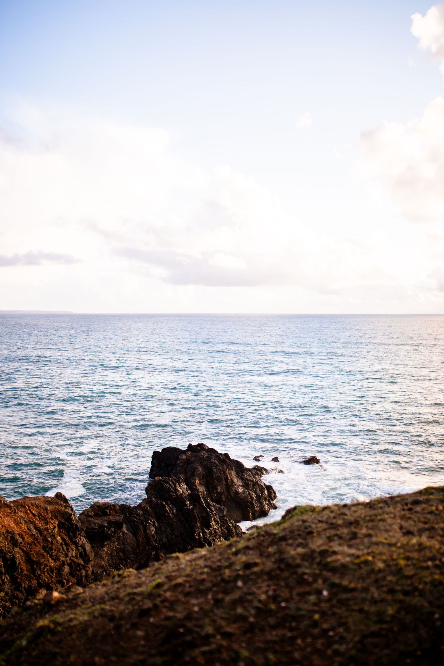 Rocky coastal outcrop against a serene blue ocean horizon during daylight.